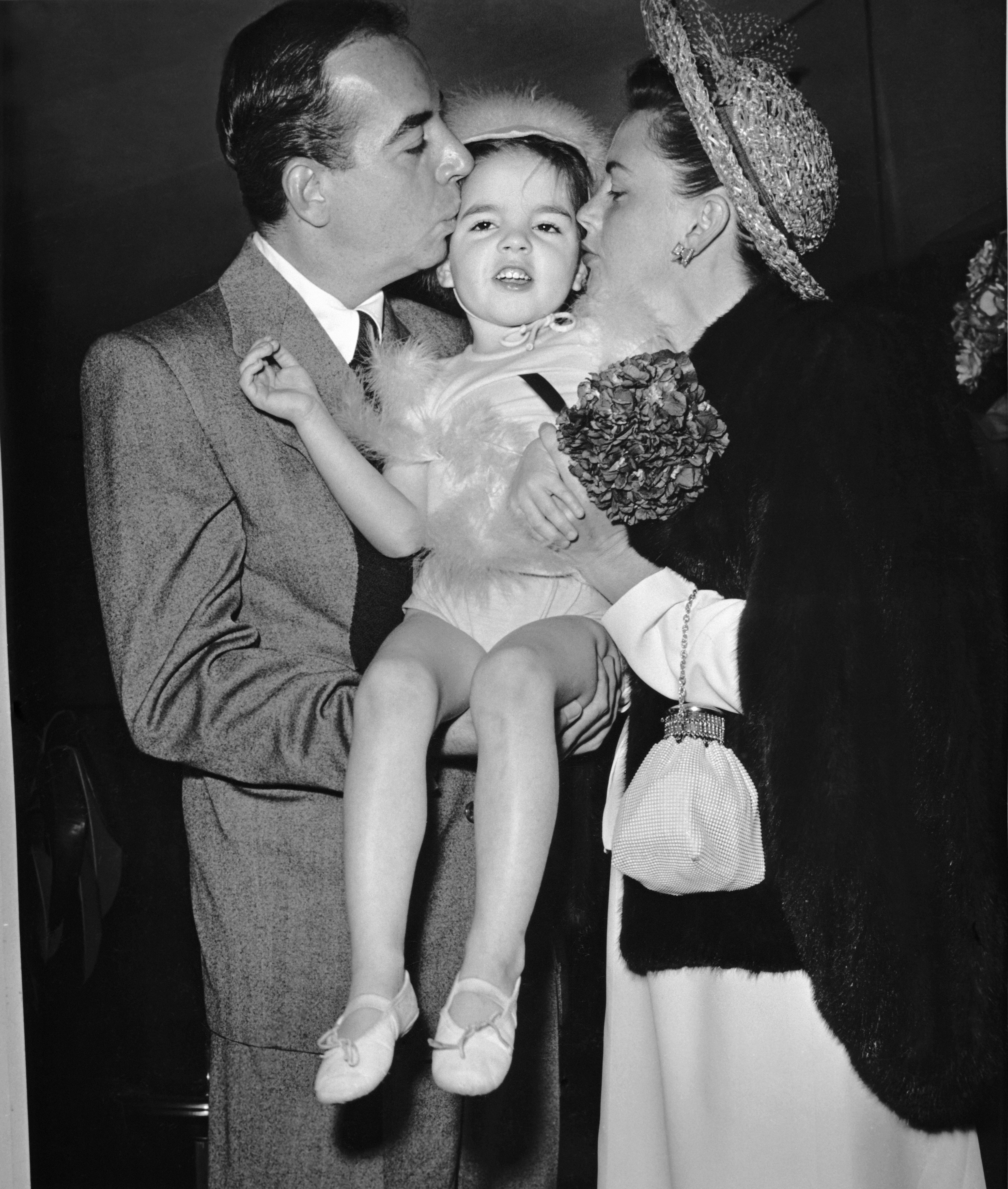 Liza Minnelli receives kisses from her mother, Judy Garland, and father, Vincente Minnelli, in April 1947 in Hollywood, California. | Source: Getty Images