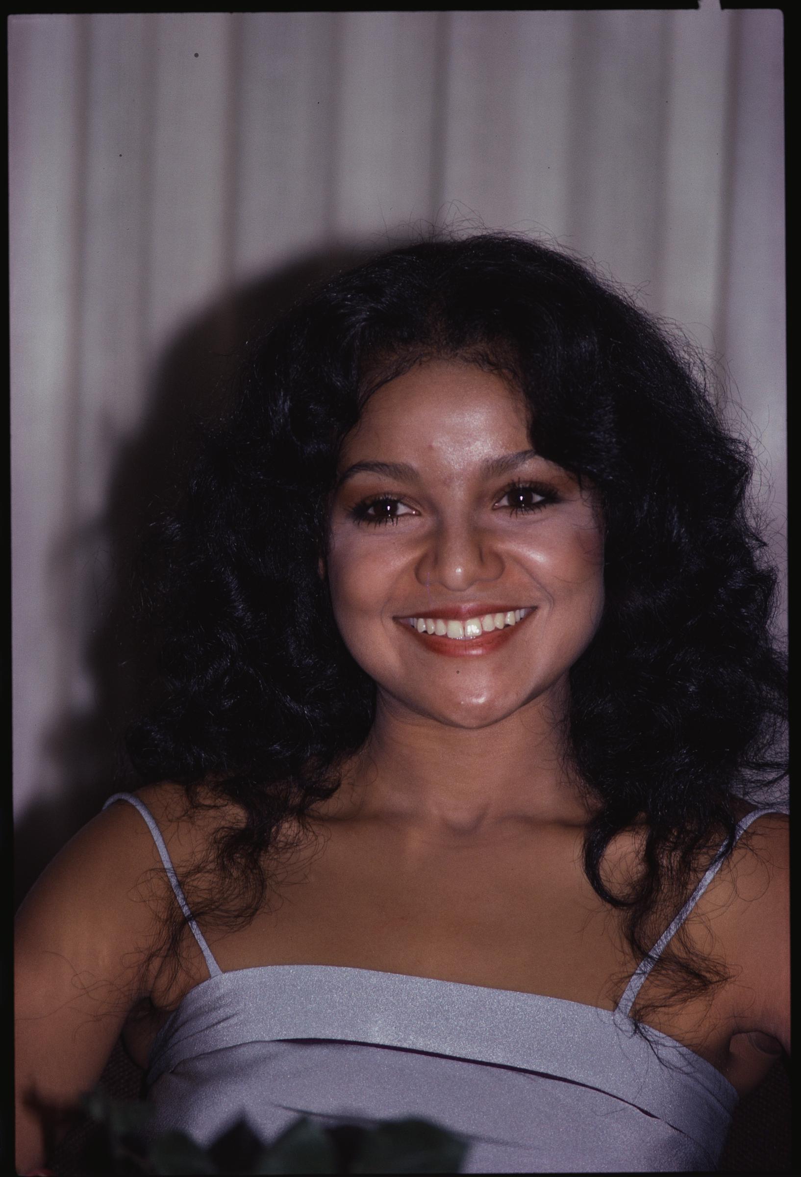 Captured in a candid moment, La Toya Jackson flashes a wide smile while wearing a silver spaghetti-strap top. Her radiant glow and soft curls highlight her natural beauty during her rise as a solo pop star.