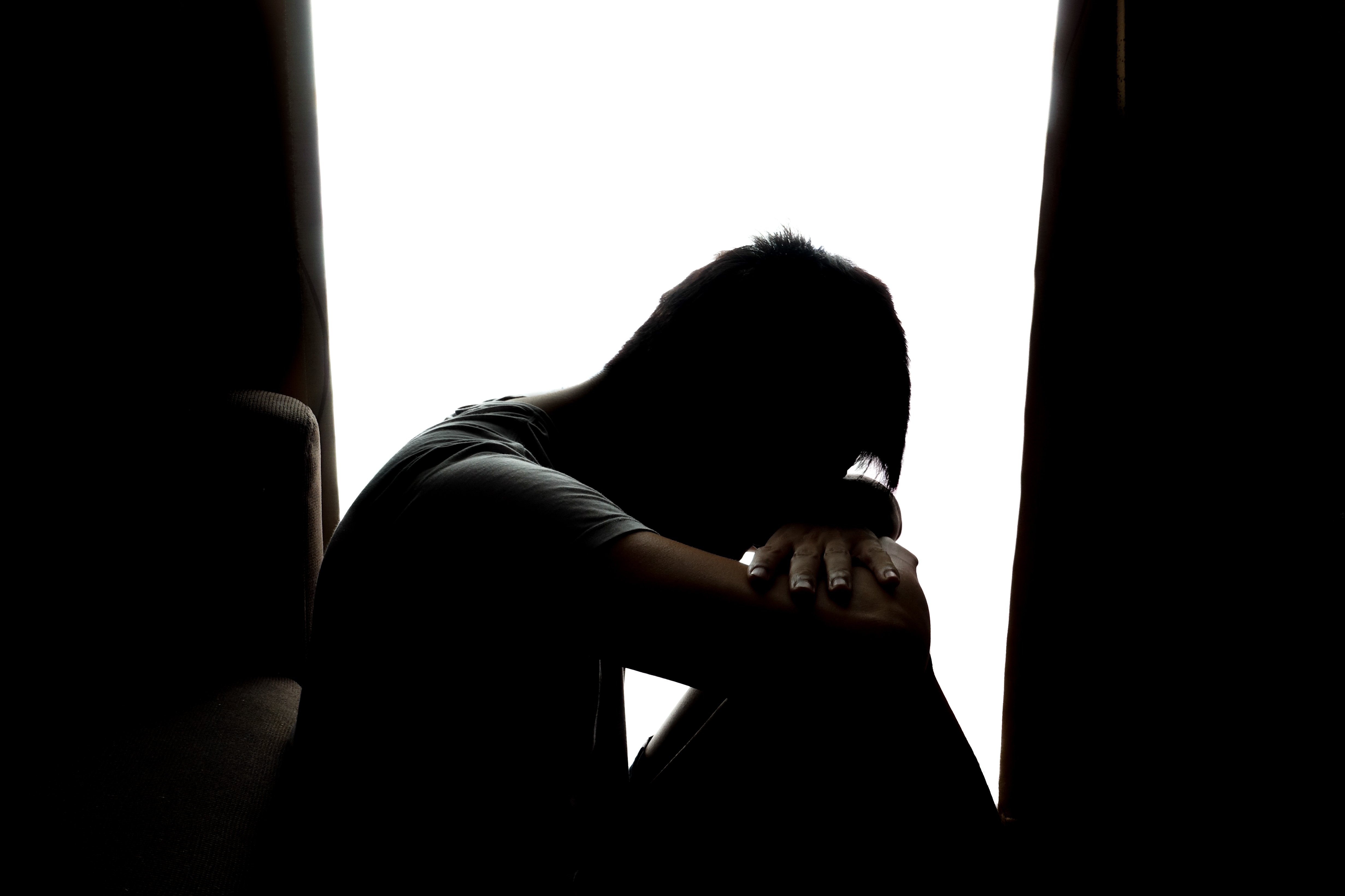 A sad boy putting his forehead on his knees with his arms crossed. │Source: Shutterstock