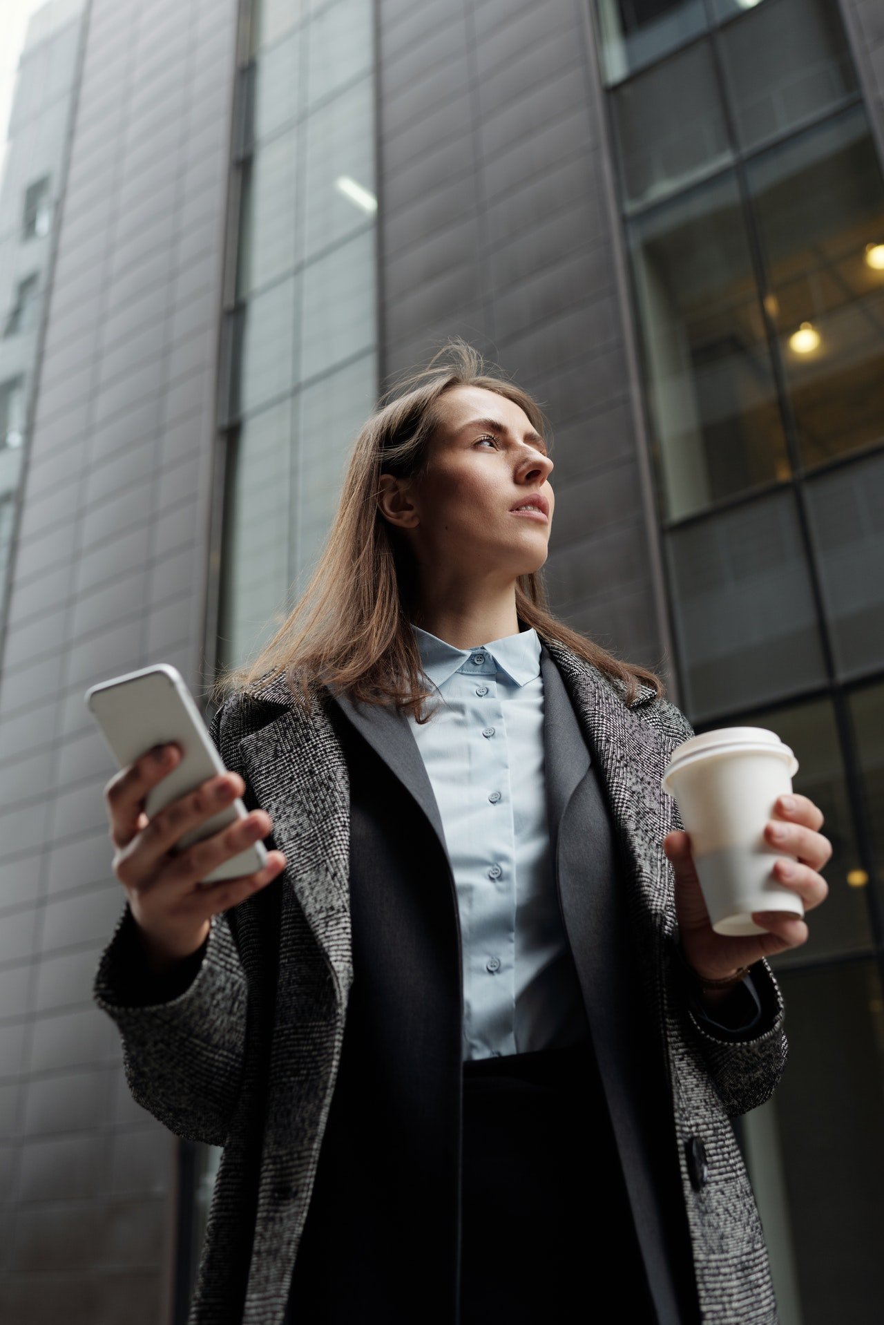 Mujer caminando en la calle con un vaso de café en una mano y su celular en la otra. | Foto: Pexels