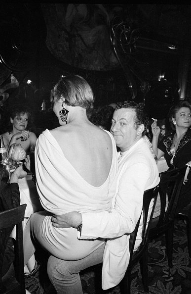 Une jeune femme assise sur les genoux de Coluche lors d'un dîner de gala le 5 avril 1983 à Paris, France. | Photo : Getty Images