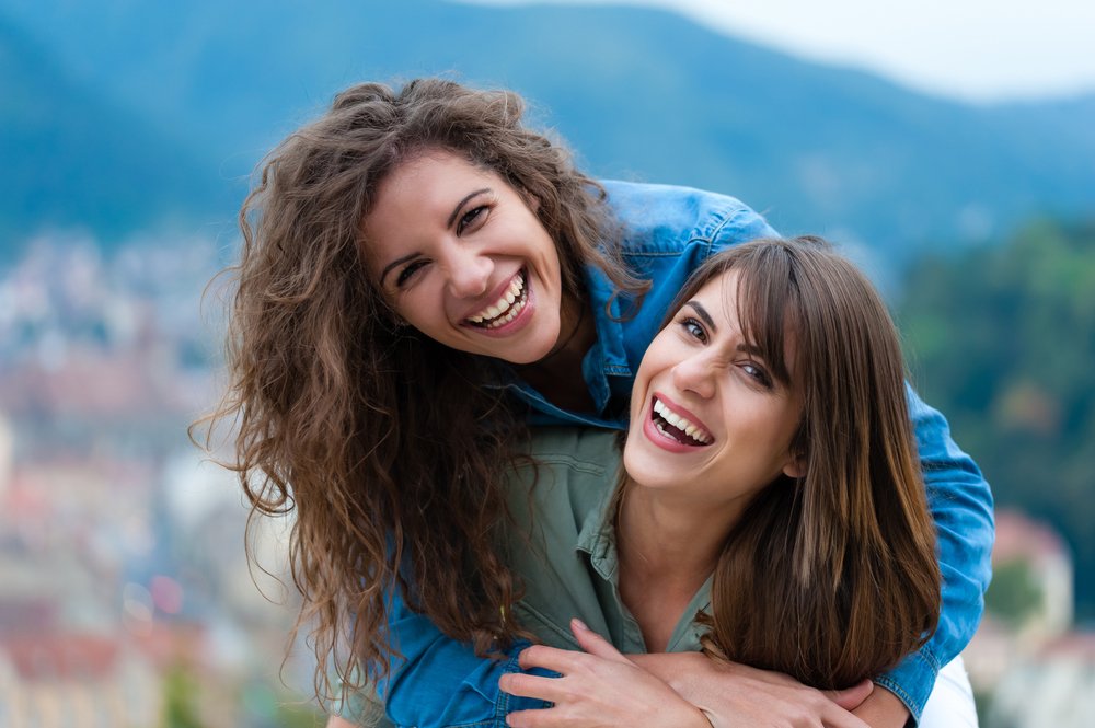 Two women friends laughing and hugging outdoors | Photo: Shutterstock/Vlad Teodor