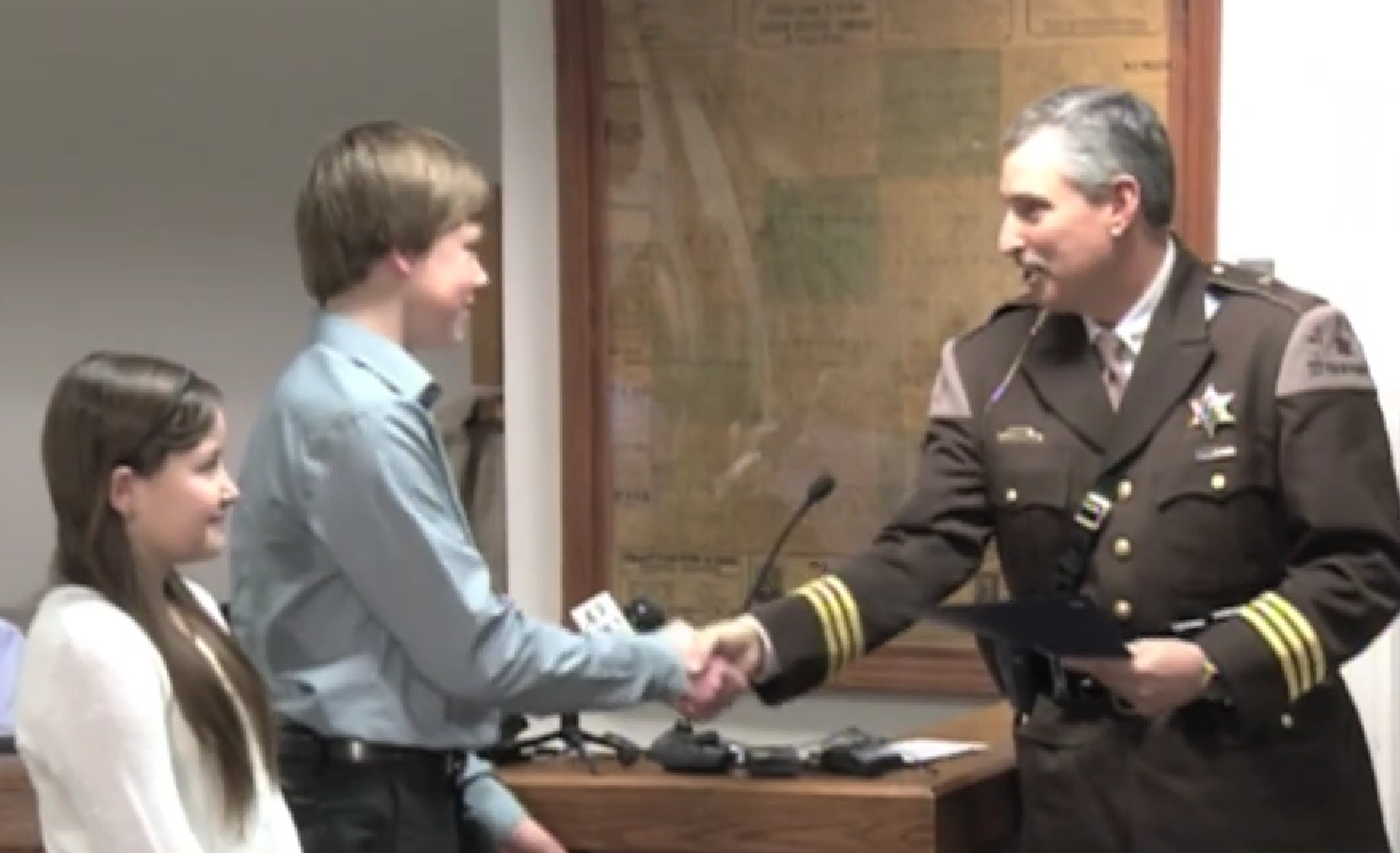 James Persyn III shaking County Sheriff Leo Mioduszewsk's hand with his sister Acelin Persyn by his side.┃Source: youtube.com/Mid-Michigan now on FOX66 & NBC25