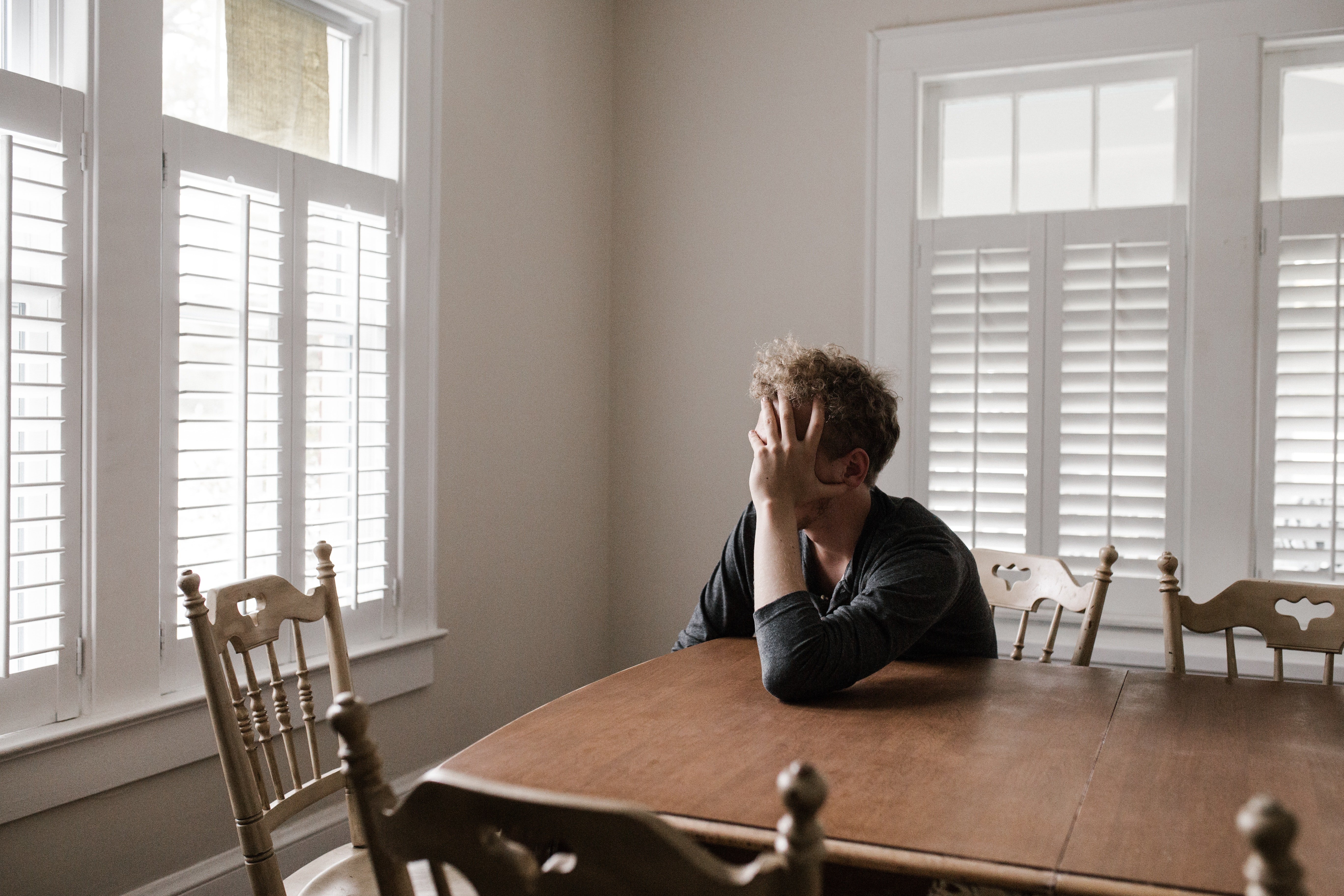 An upset man looking crushed while sitting at a table with one hand over his face | Source: Pexels