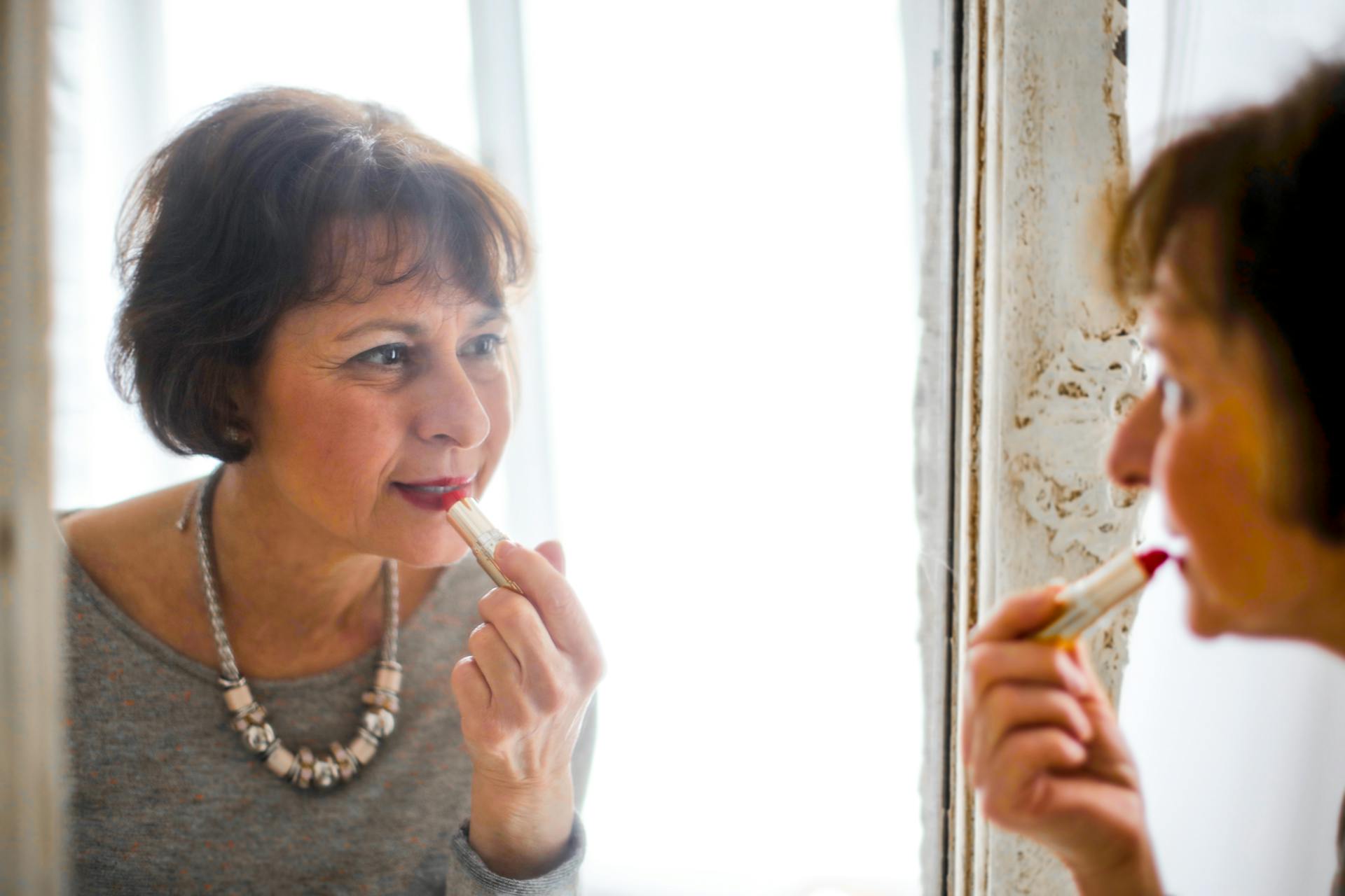 A senior woman applying lipstick in front of the mirror | Source: Pexels