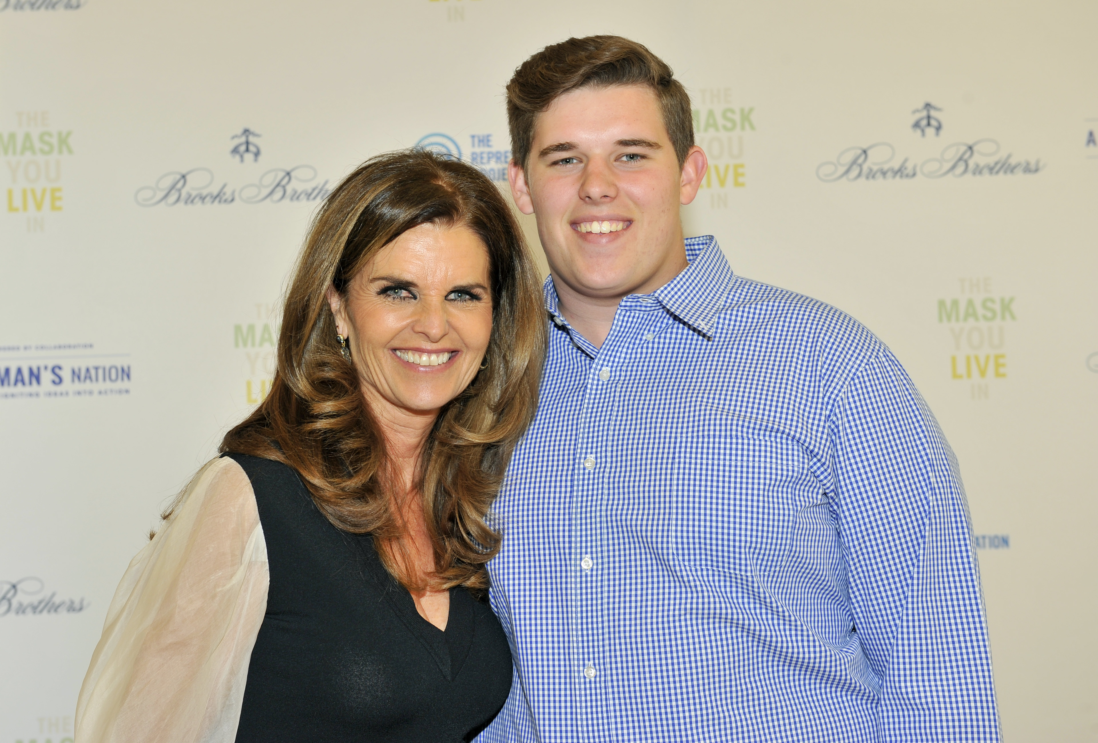 Christopher appears at the LA premiere of "The Mask You Live In" with his mother, Maria Shriver, in April 2015. Wearing a neatly pressed blue checkered shirt, he stands with a broad smile and a clean-cut hairstyle, reflecting a polished and composed look during his late teens.