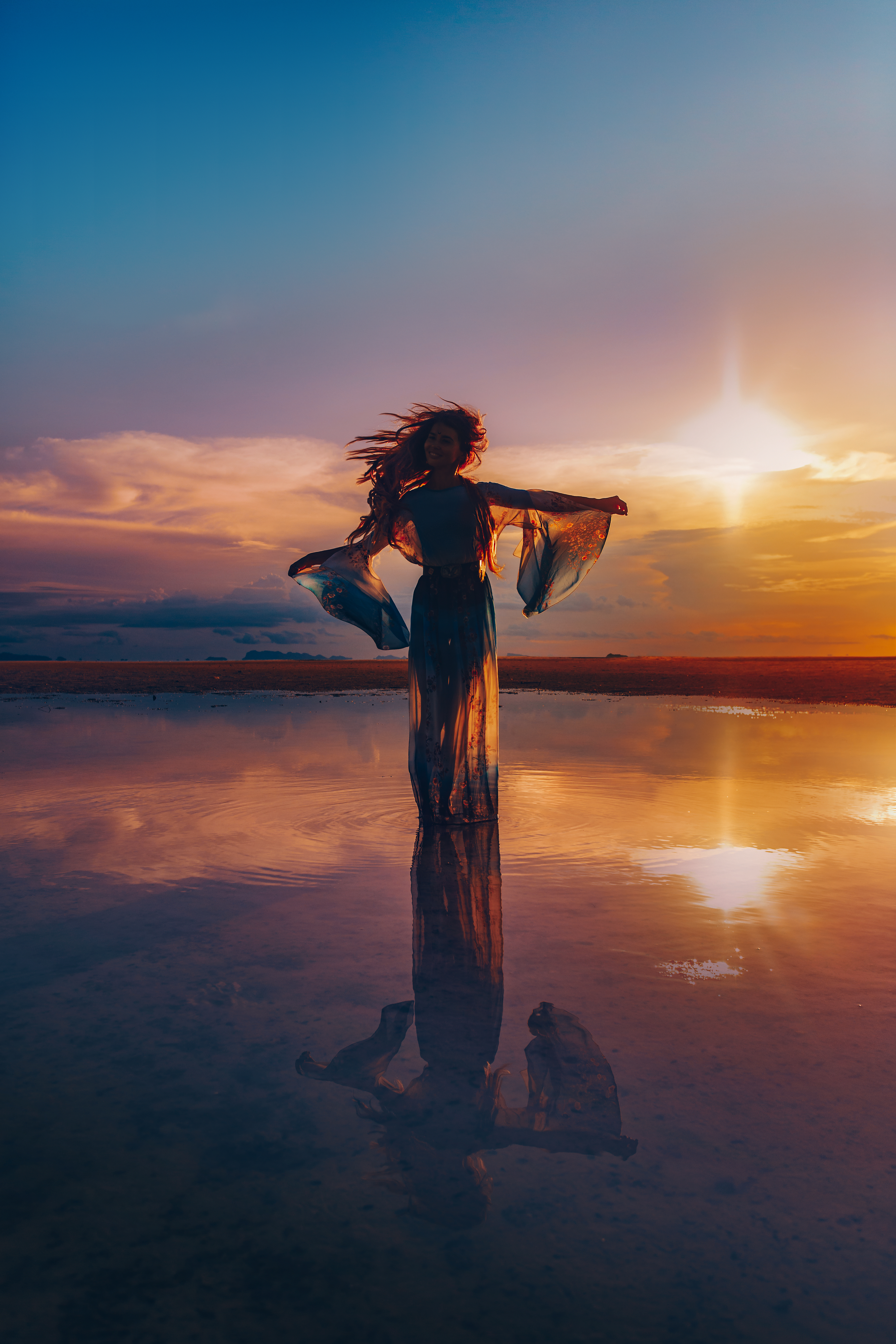 A portrait of a woman standing in the middle of a pond with her arms spread out during a sunset | Source: Shutterstock