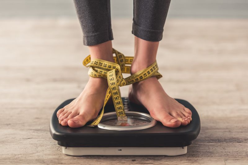 A person on a weighing scale and tape measure. | Source: Getty Images