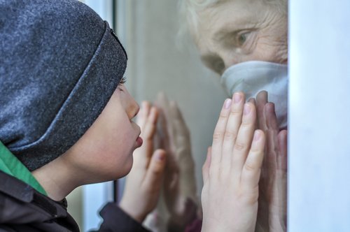 Großmutter mit Gesichtsmaske und Kind halten Hände durch Fensterscheibe | Quelle: Shutterstock