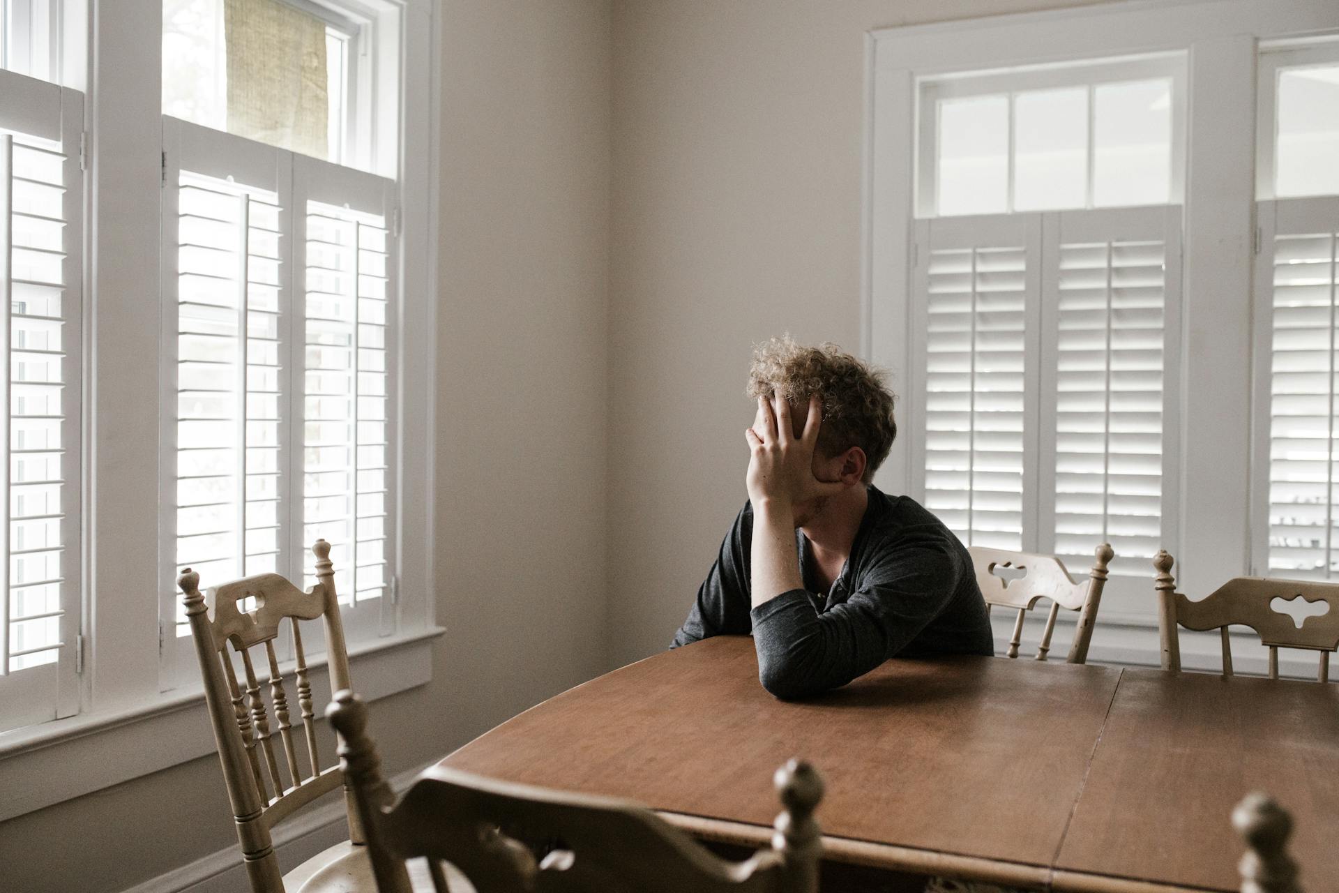 A young guy leaning on a wooden table while hiding his face | Source: Pexels