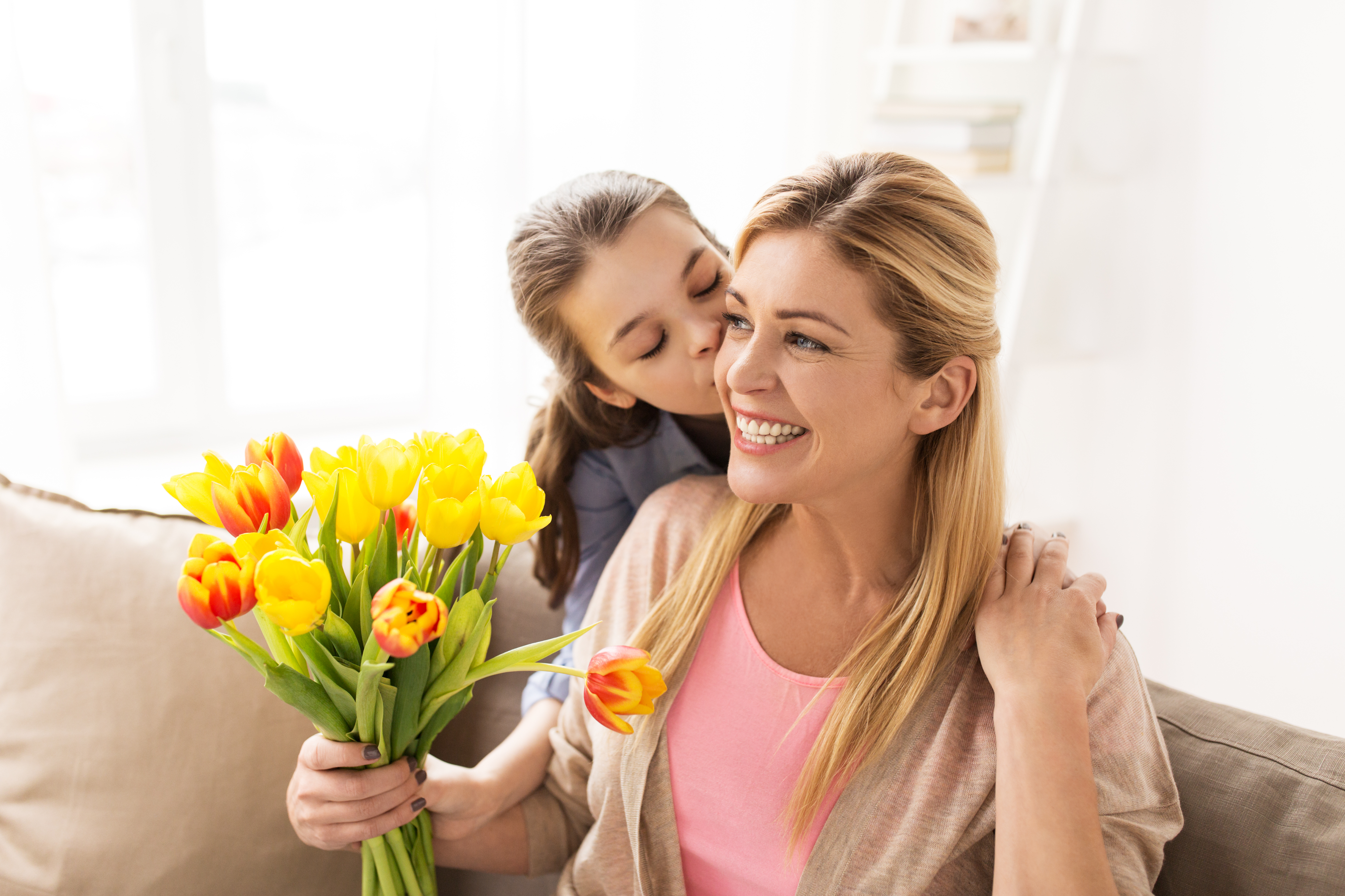 A teenage girl kisses her mother and gives her flowers | Source: Shutterstock
