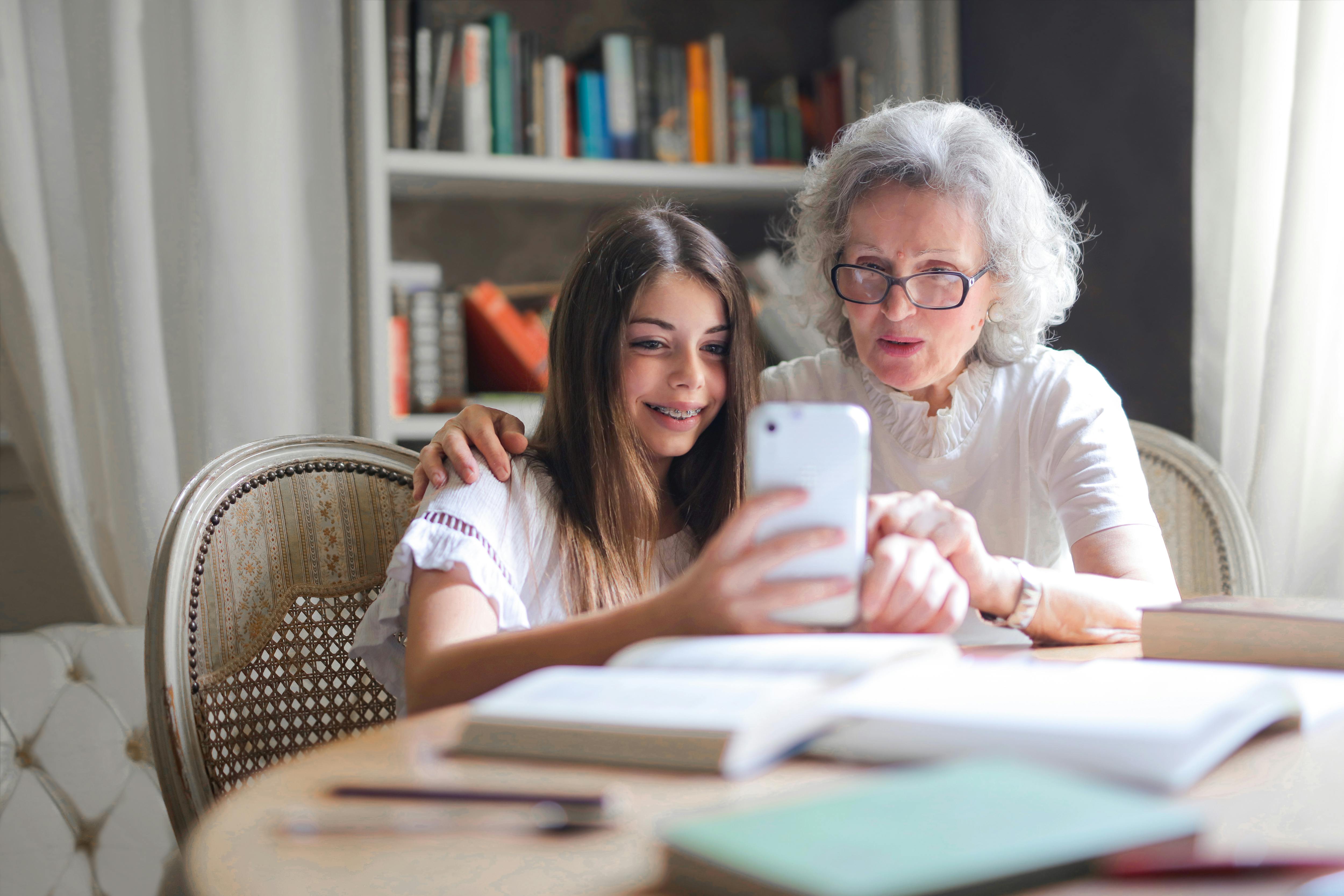 A happy little girl bonding with her grandmother while using a phone | Source: Pexels