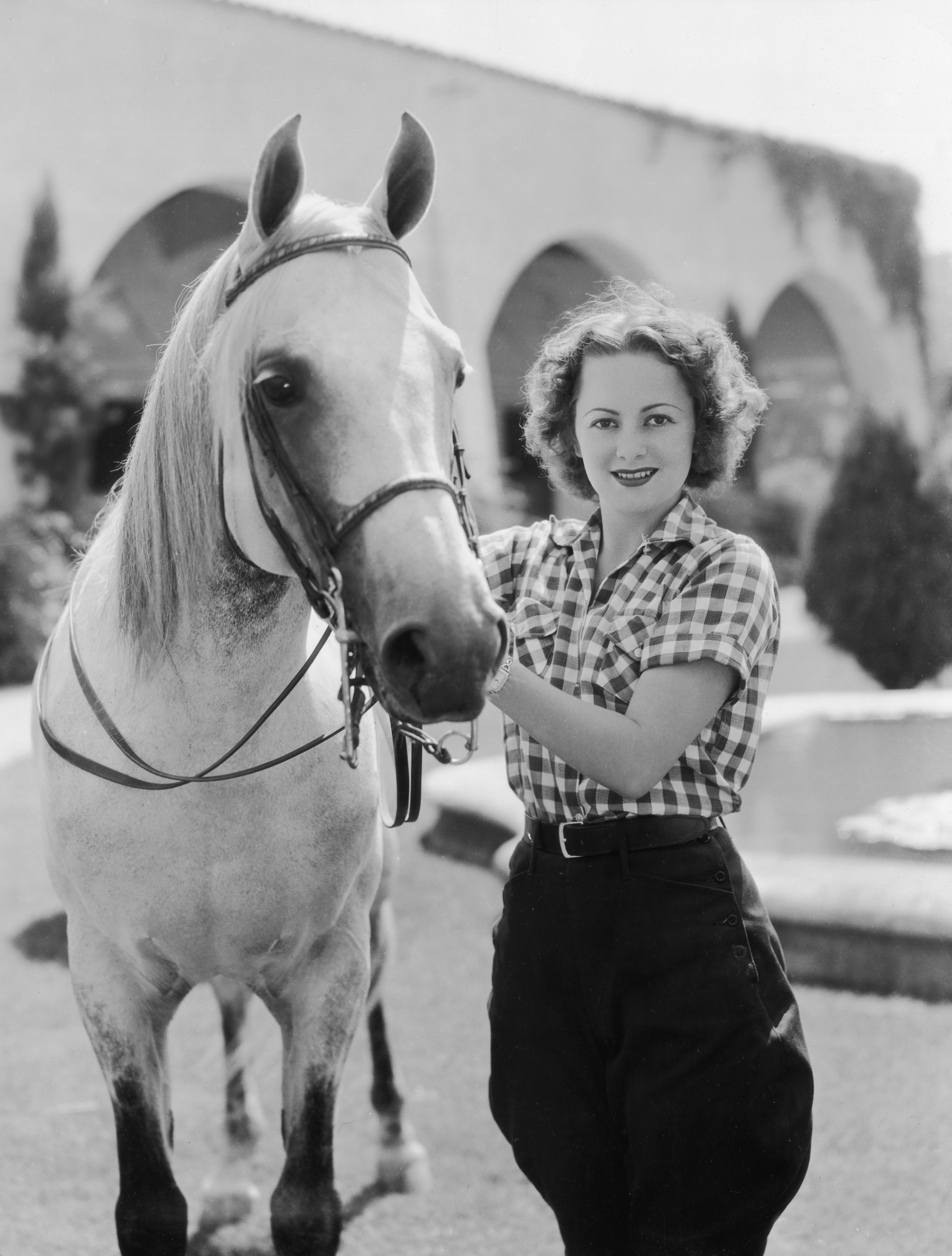 Actress Olivia de Havilland stands next to a horse and holds its reigns in front of cloisters and a fountain. Circa 1935 | Source: Getty Images