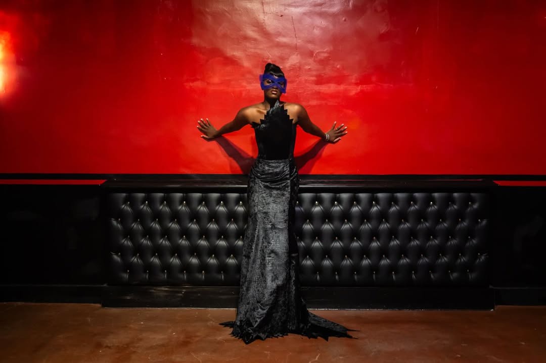 Zaya Wade strikes a theatrical pose in a black gown and blue mask, framed by a vivid red wall and tufted black backdrop during the Translatable Ball. | Source: Instagram/translatableproject