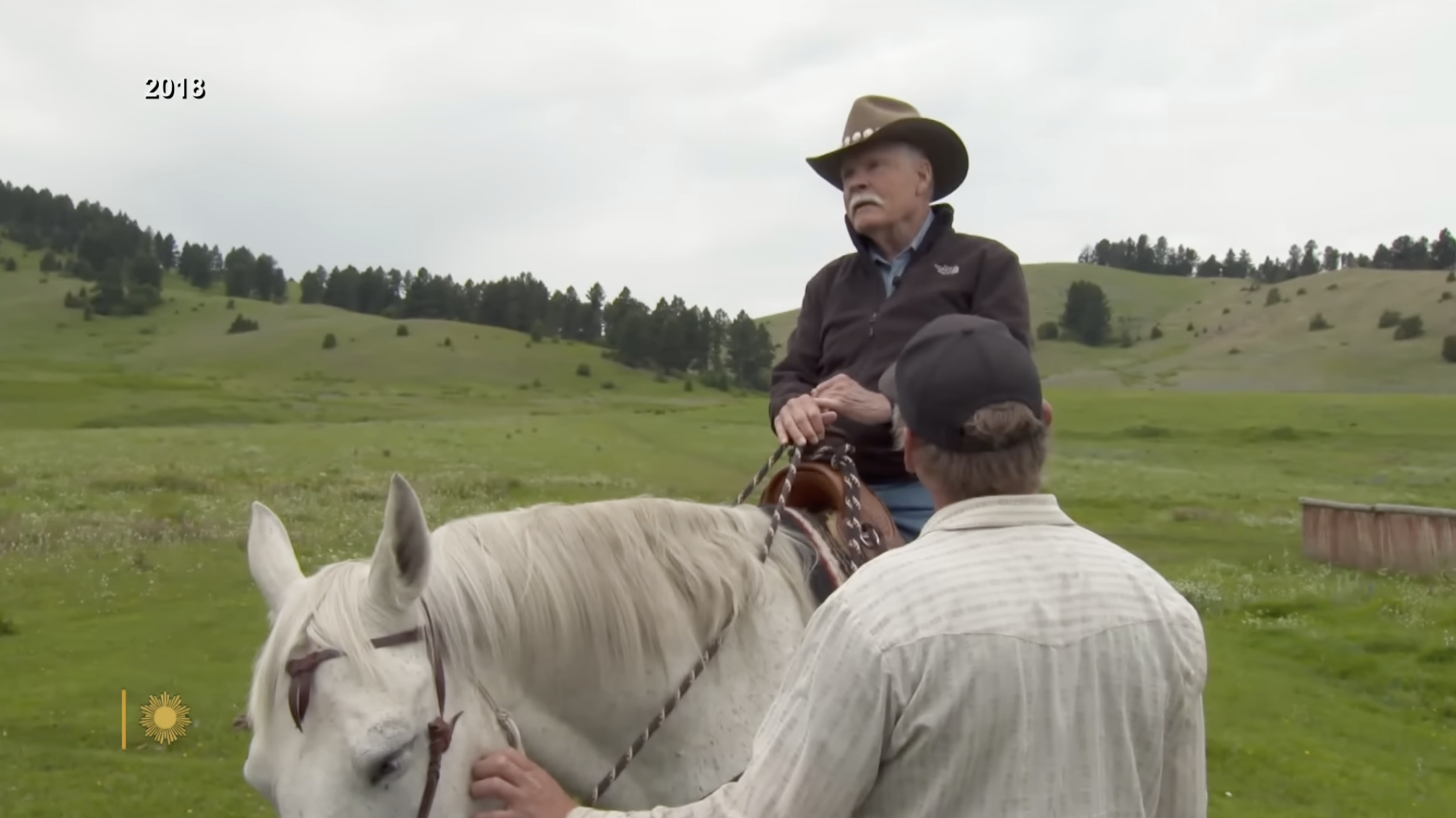 Ted Turner rides horseback through open green fields, embracing the ranching lifestyle that has become central to his conservation mission. | Source: YouTube/CBS Sunday Morning