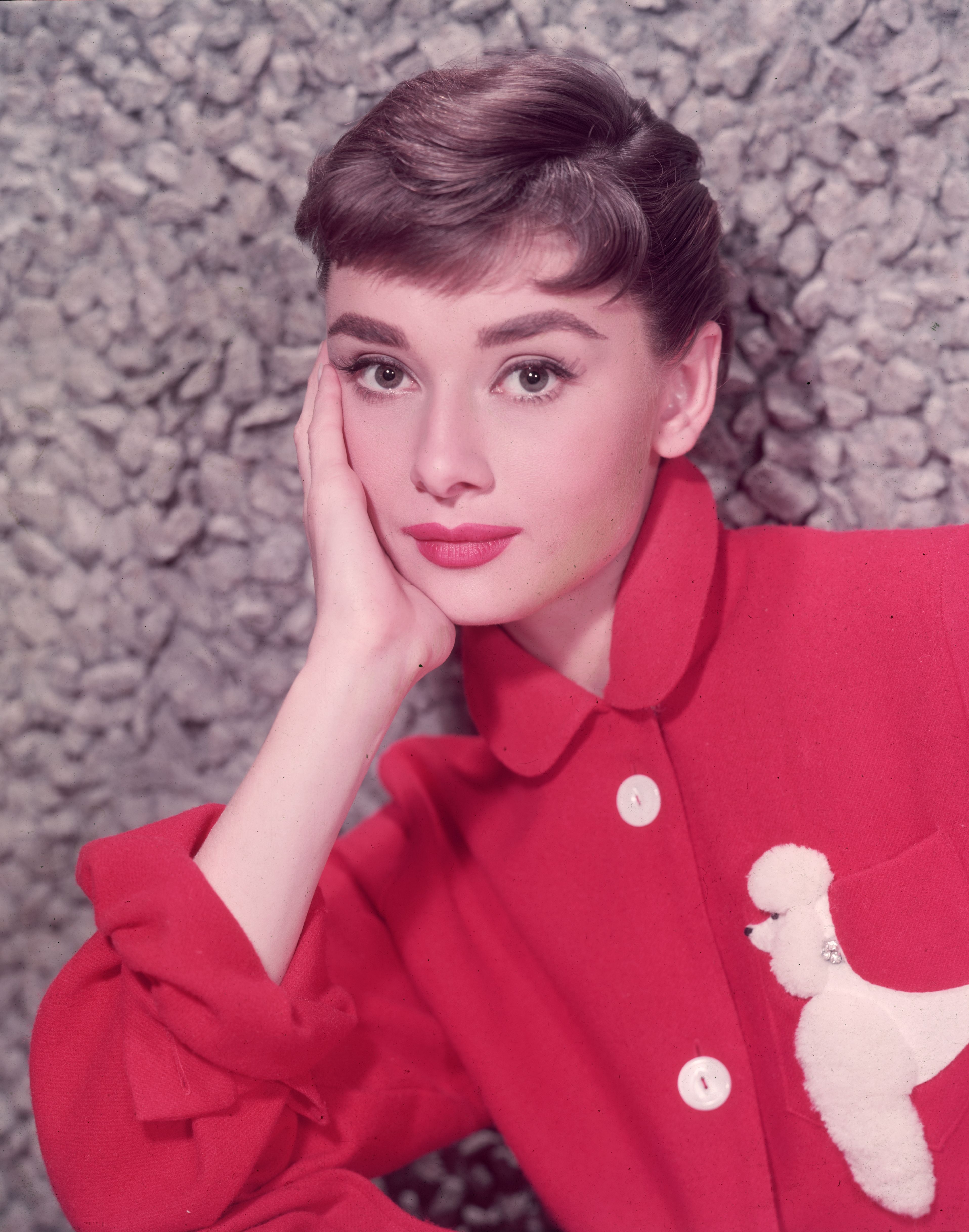 Porträt des in Belgien geborenen Schauspielers Audrey Hepburn (1929 - 1993), der sich in einer roten Jacke mit einer Pudelapplikation auf ihre Hand stützt. (Foto von Hulton Archive) I Quelle: Getty Images