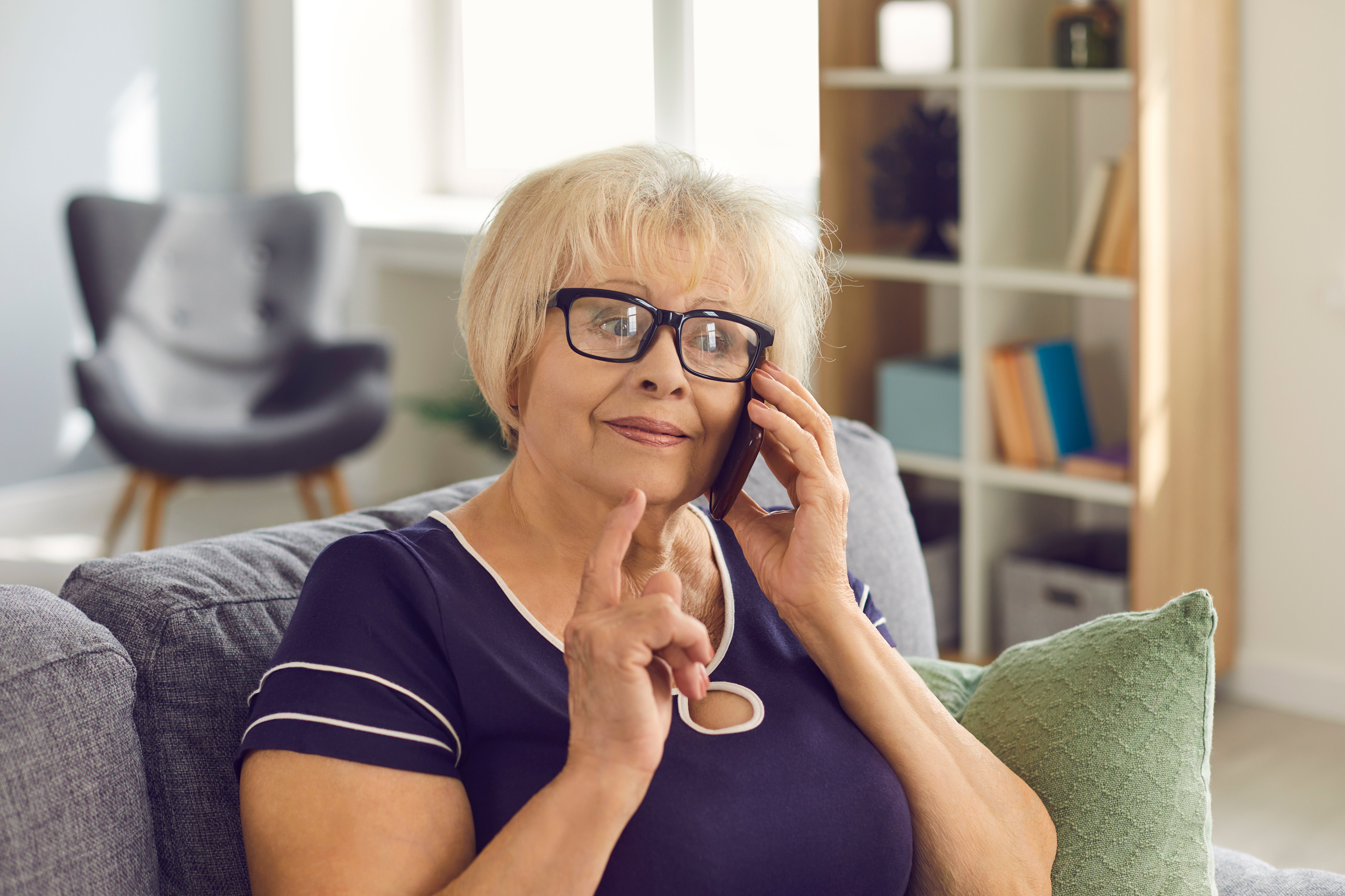 An older woman wearing glasses while sitting on a couch and speaking on a phone | Source: Shutterstock
