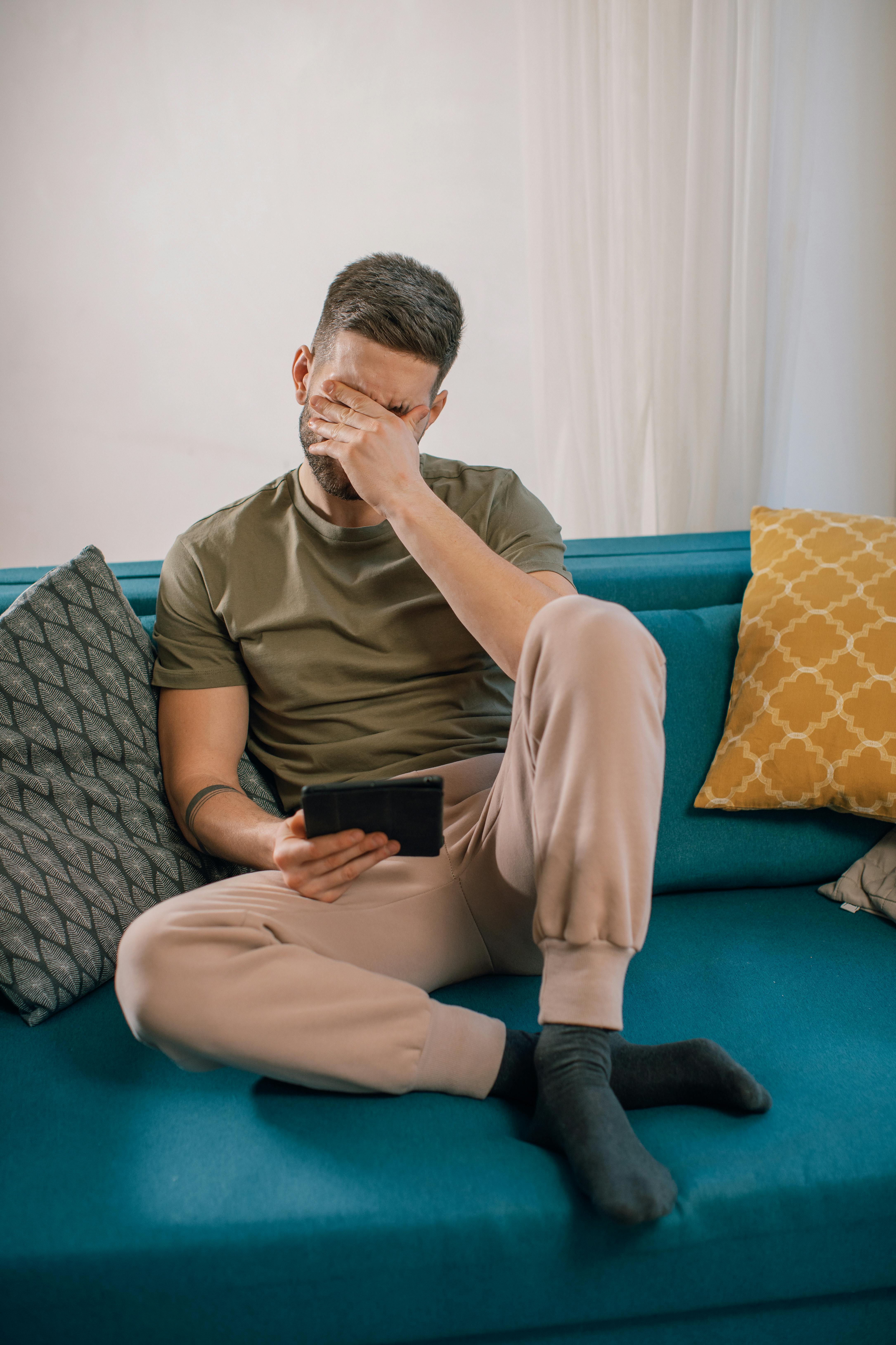 An man sitting on a couch, his hand covering a part of his face | Source: Pexels