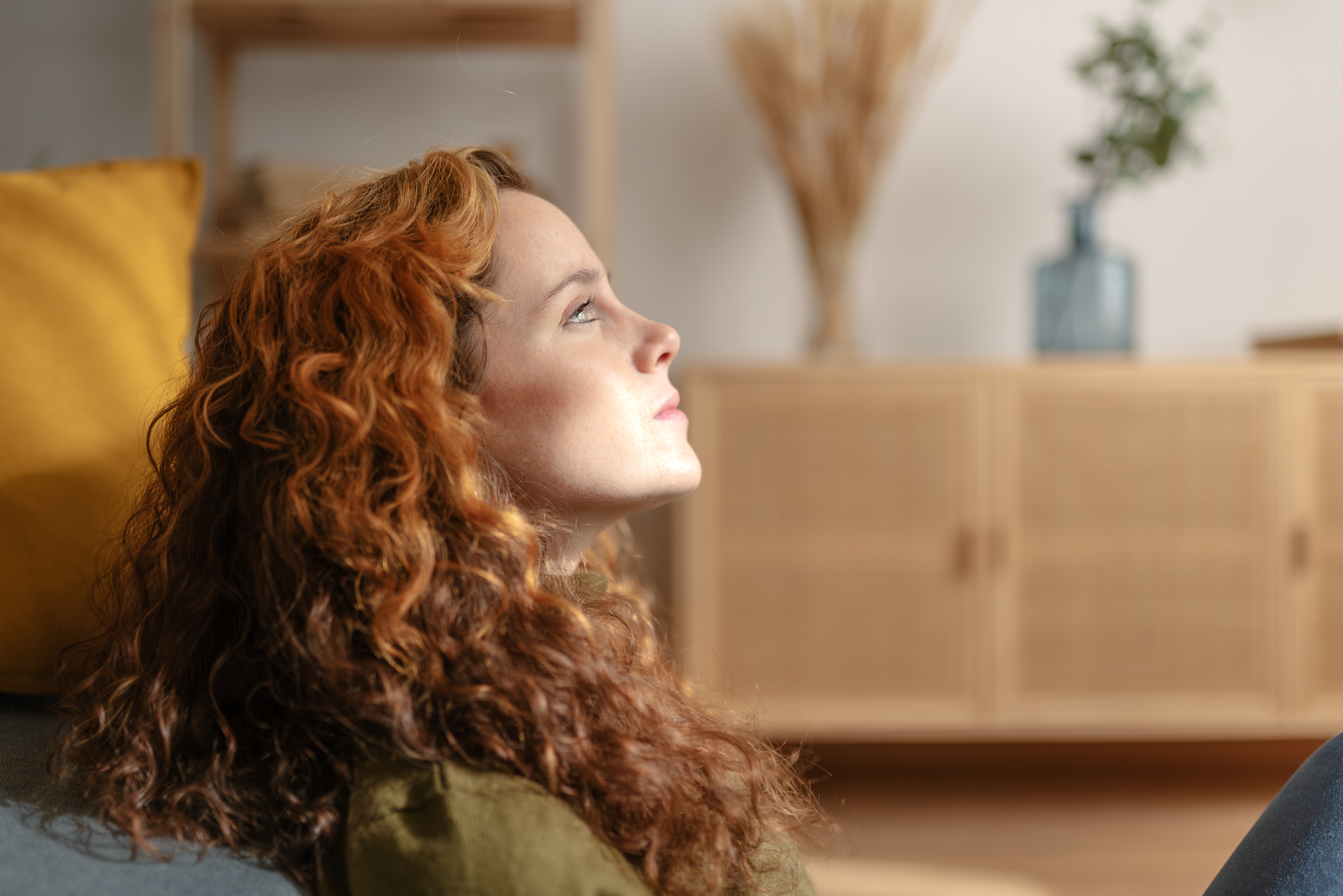 Close up view of a young redhead woman sitting on the floor, leaning her back on sofa and looking into the distance with sad face | Source: Getty Images