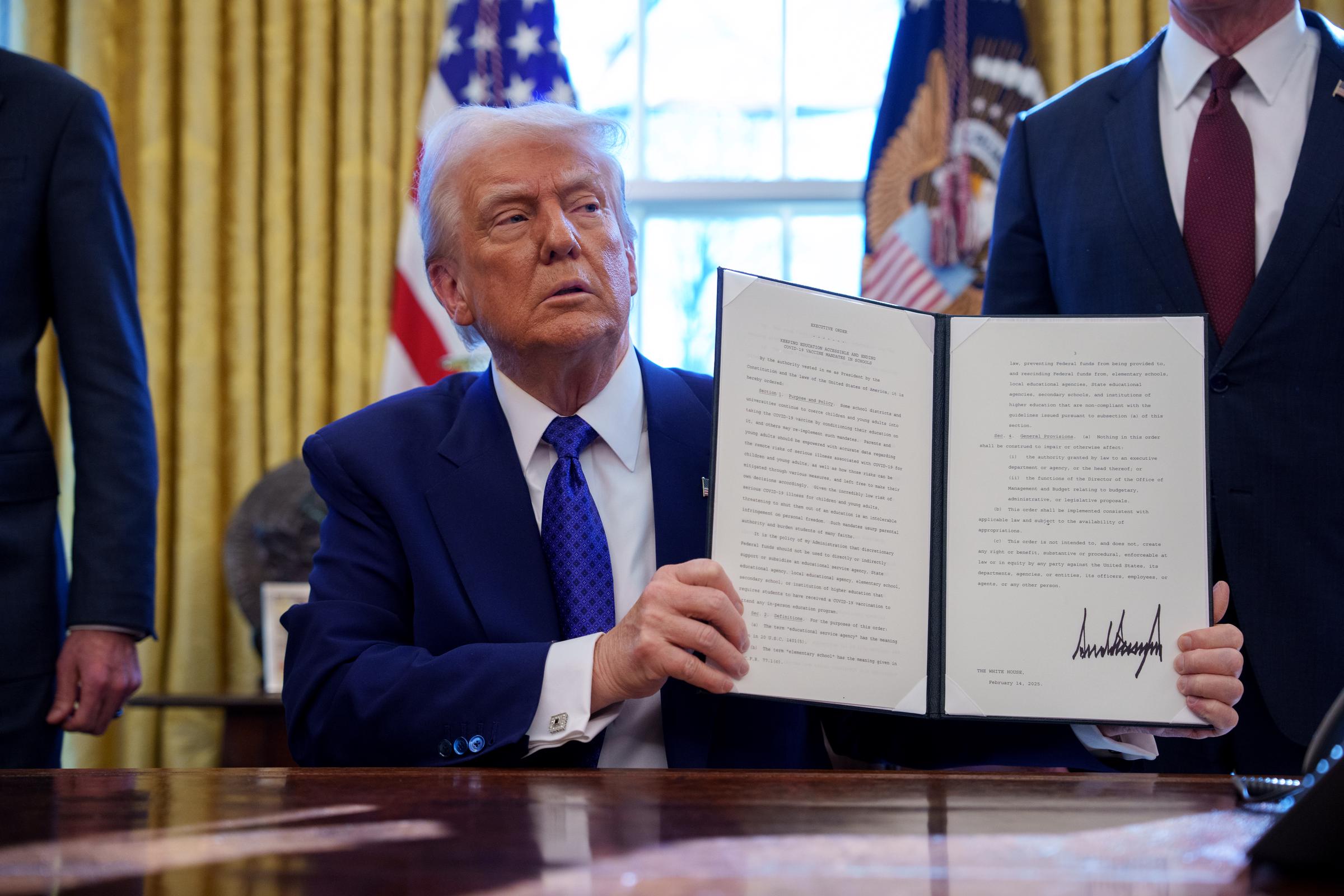 U.S. President Donald Trump signs an executive order withholding federal funding from schools and universities that impose a COVID-19 vaccine mandate in the Oval Office at the White House on February 14, 2025, in Washington, DC | Source: Getty Images