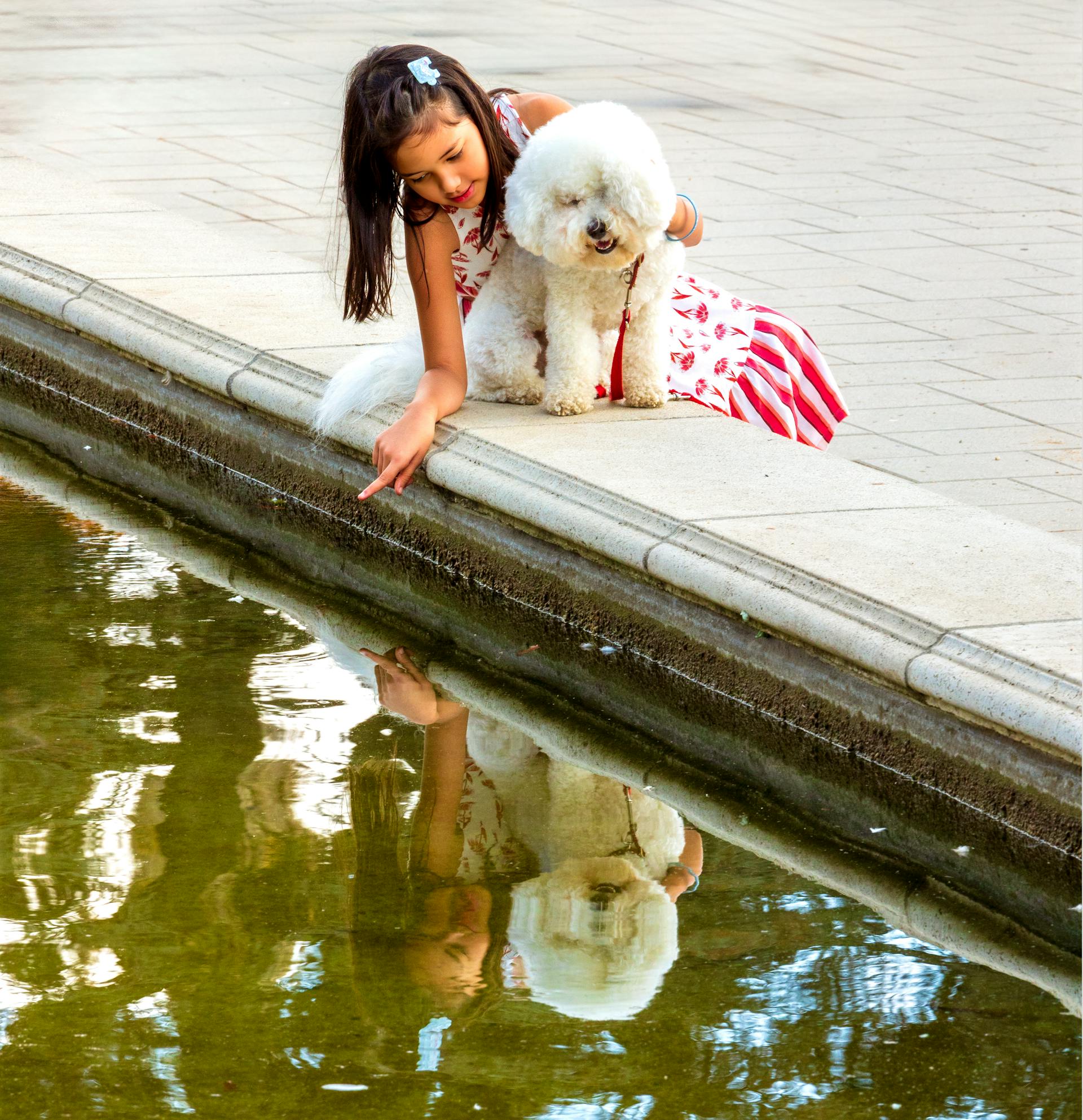 A little girl sitting next to a fountain with her dog | Source: Pexels