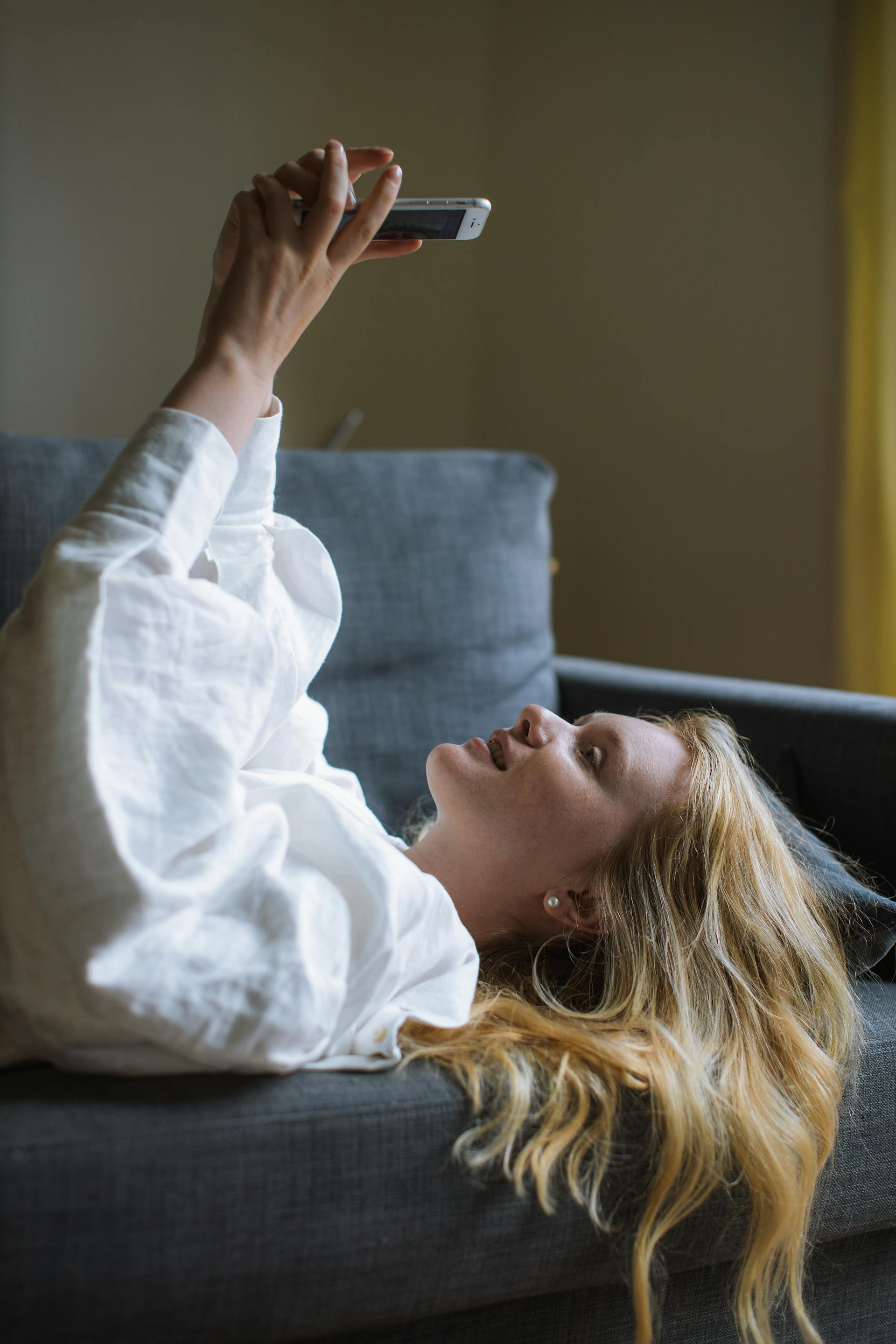A young woman using her phone while lying on a sofa | Source: Pexels