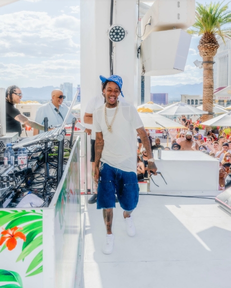 Wiz Khalifa walks through a venue while wearing a white T-shirt, blue shorts, and a blue cap in a post dated May 15, 2025. | Source: Facebook/Wiz Khalifa