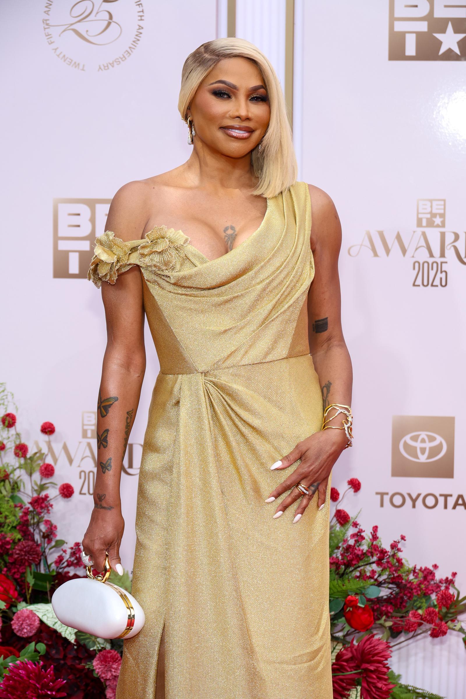 Sandra Denton radiates star power at the BET Awards, gliding onto the Peacock Theater's even in a shimmering gold gown that drapes with sculptural elegance. Her gold-gown moment reveals the most dramatic evolution yet — the appearance that sparked today’s viral debate.