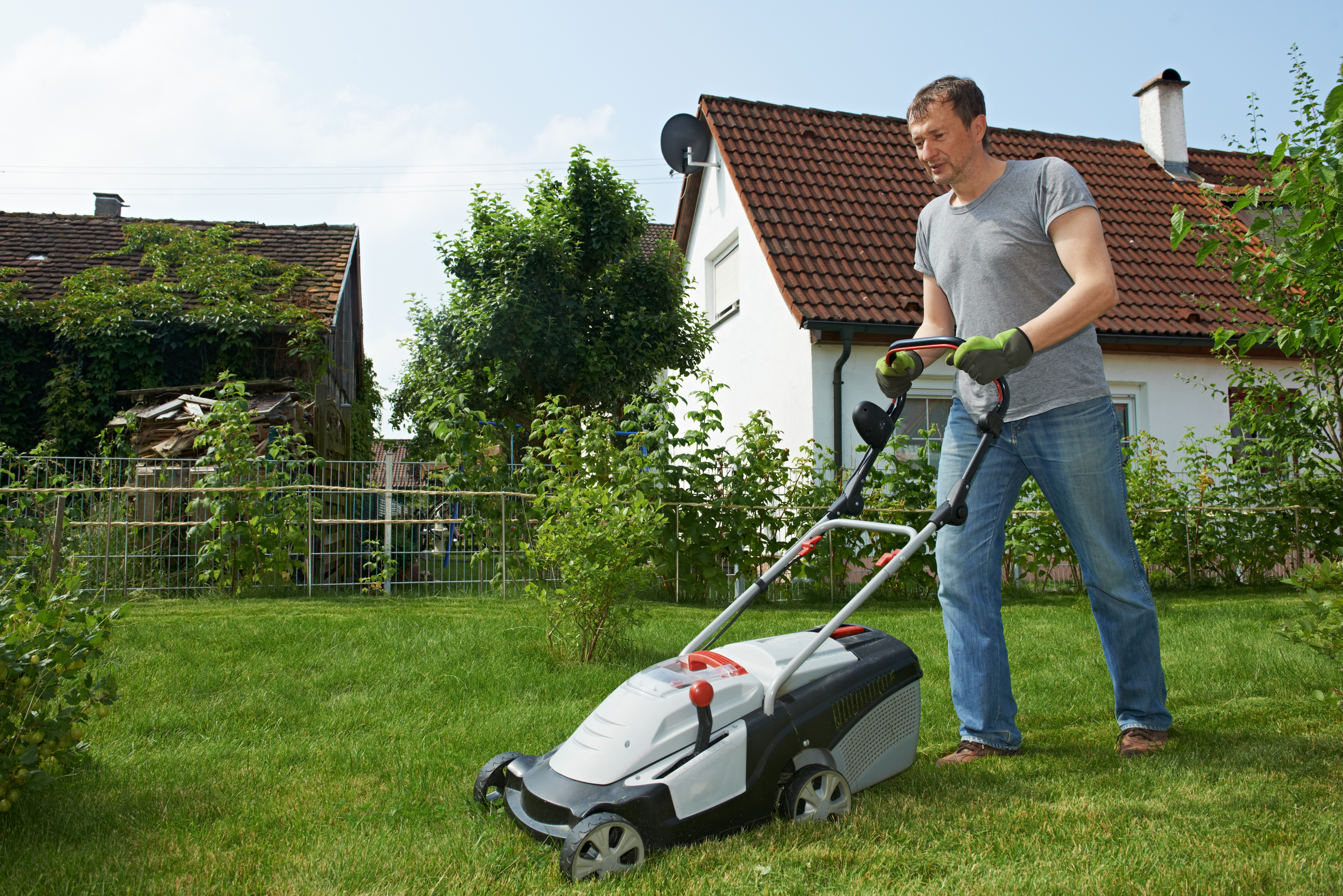Man cutting grass in his garden yard with lawn mower. | Source: Shutterstock