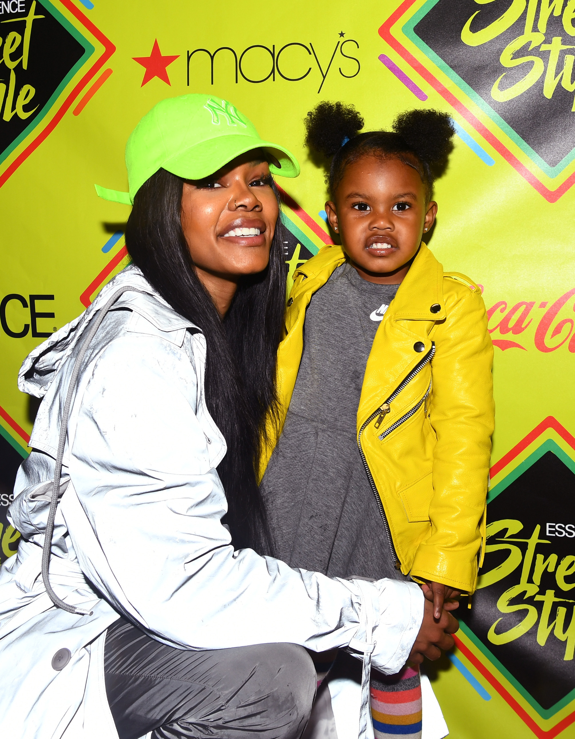 Teyana Taylor kneels beside Iman Tayla "Junie" Shumpert Jr. at the Essence Street Style Festival in Brooklyn. Teyana wears a neon cap while Junie stands out in a bright yellow jacket.