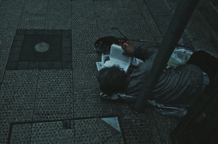 Un pauvre enfant seul,dans la rue,qui lit un livre | Photo : Unsplash