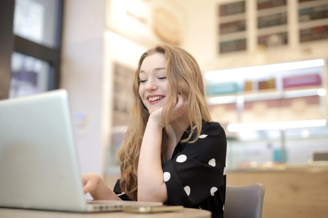 Mujer joven sonriendo mientras ve la pantalla de una laptop. | Foto: Pexels