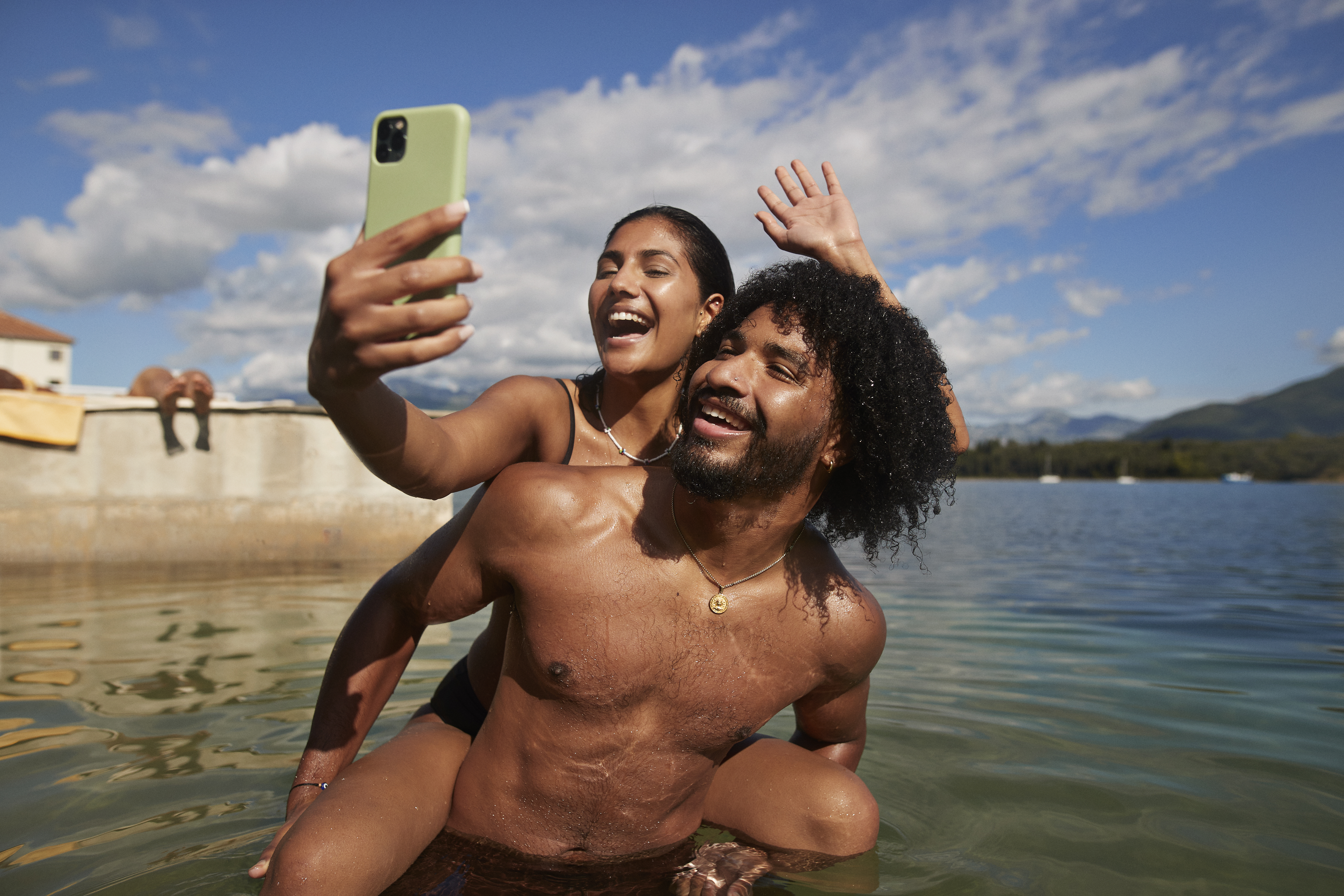 A happy woman taking selfie while her boyfriend gives her piggybackride at a bay. | Source: Getty Images