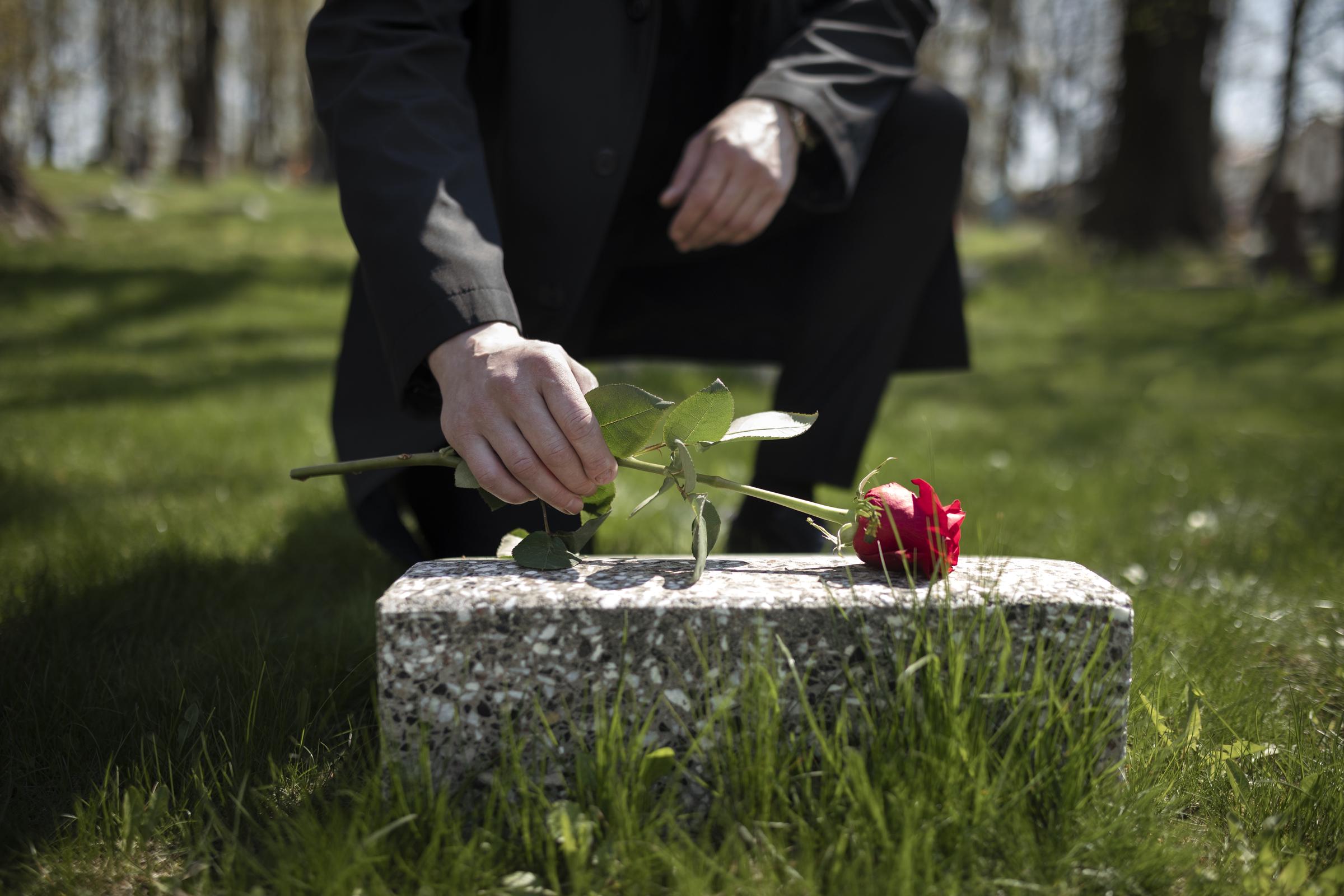 Man keeping a rose on a tombstone | Source: Freepik