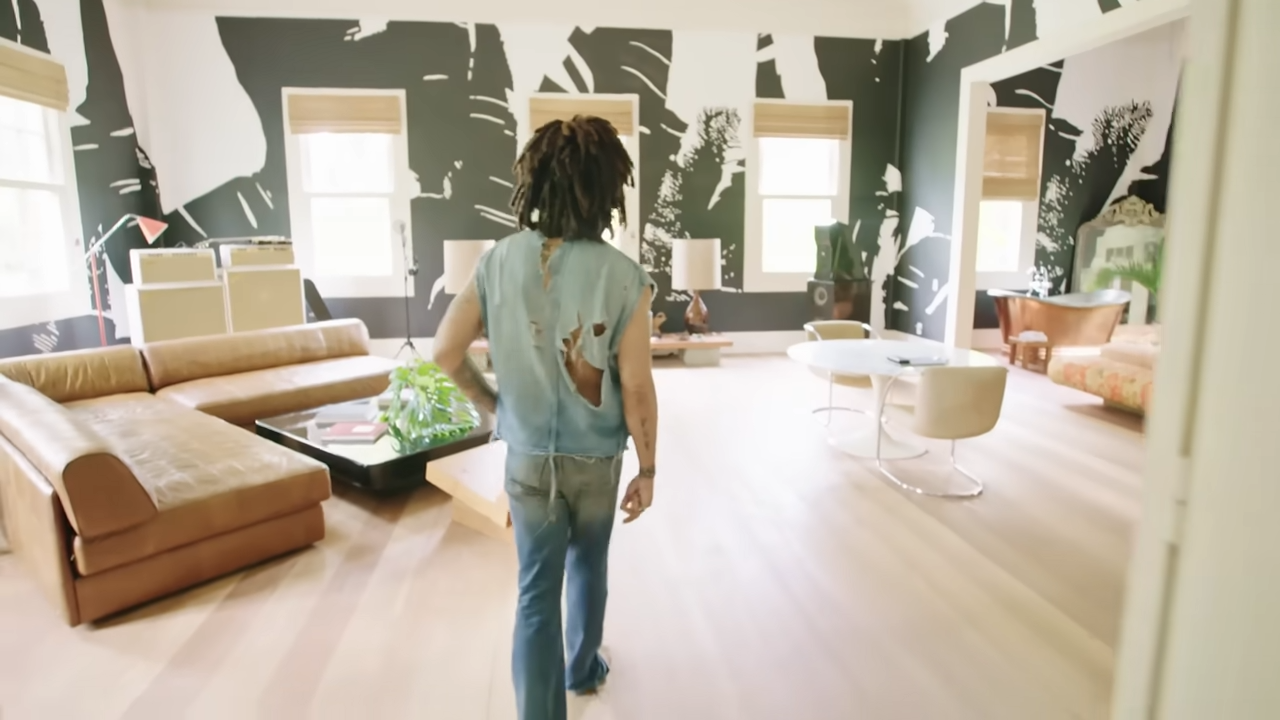 Lenny walks into the spacious, open-concept master bedroom suite, showing off the back of his shredded denim shirt. | Source: YouTube/@Archdigest