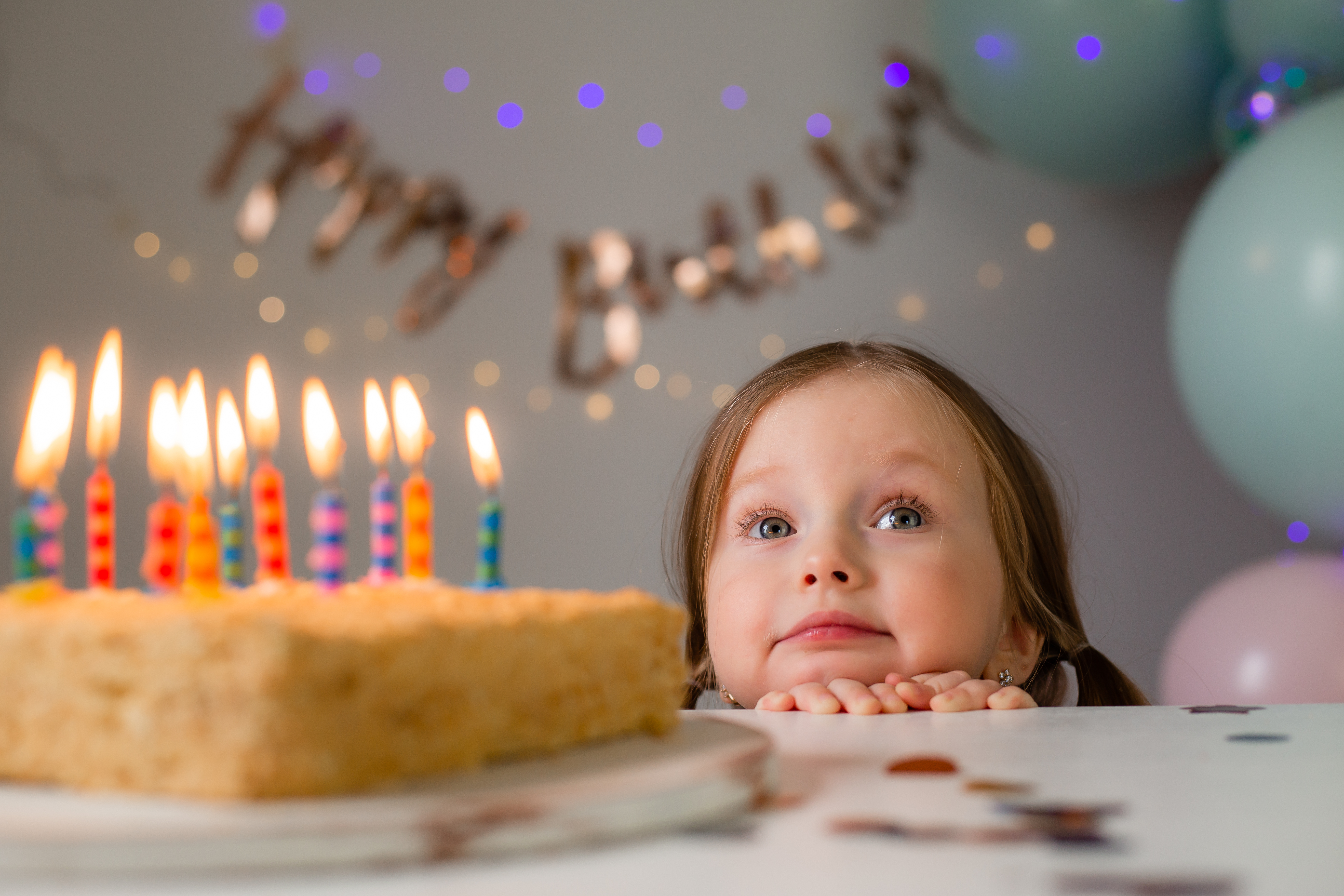 A young girl peeping over a table with a birthday cake | Source: Shutterstock