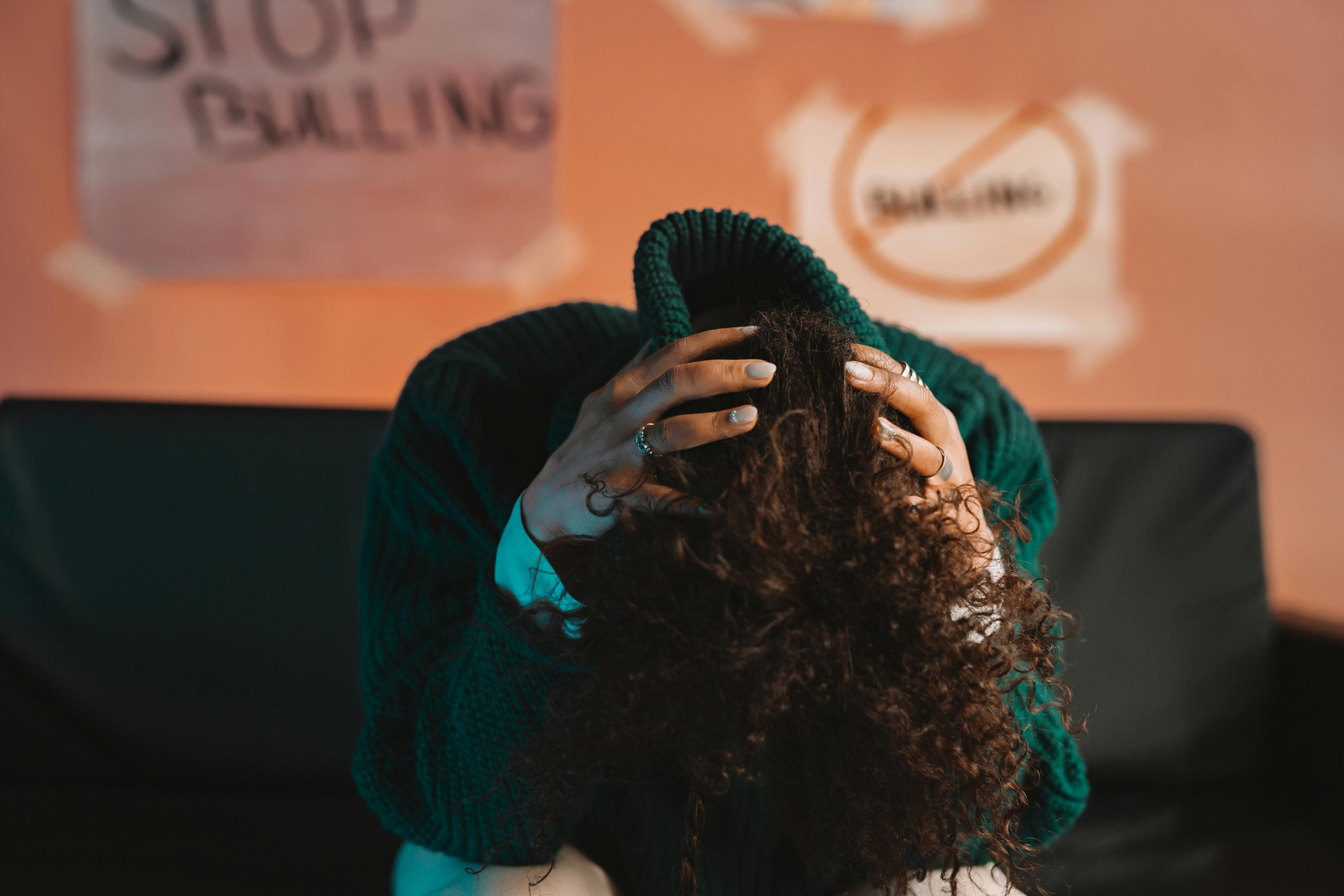 A student sits with their head in their hands beneath a "Stop Bullying" sign, symbolising the mental toll associated with ongoing mistreatment. | Source: Pexels