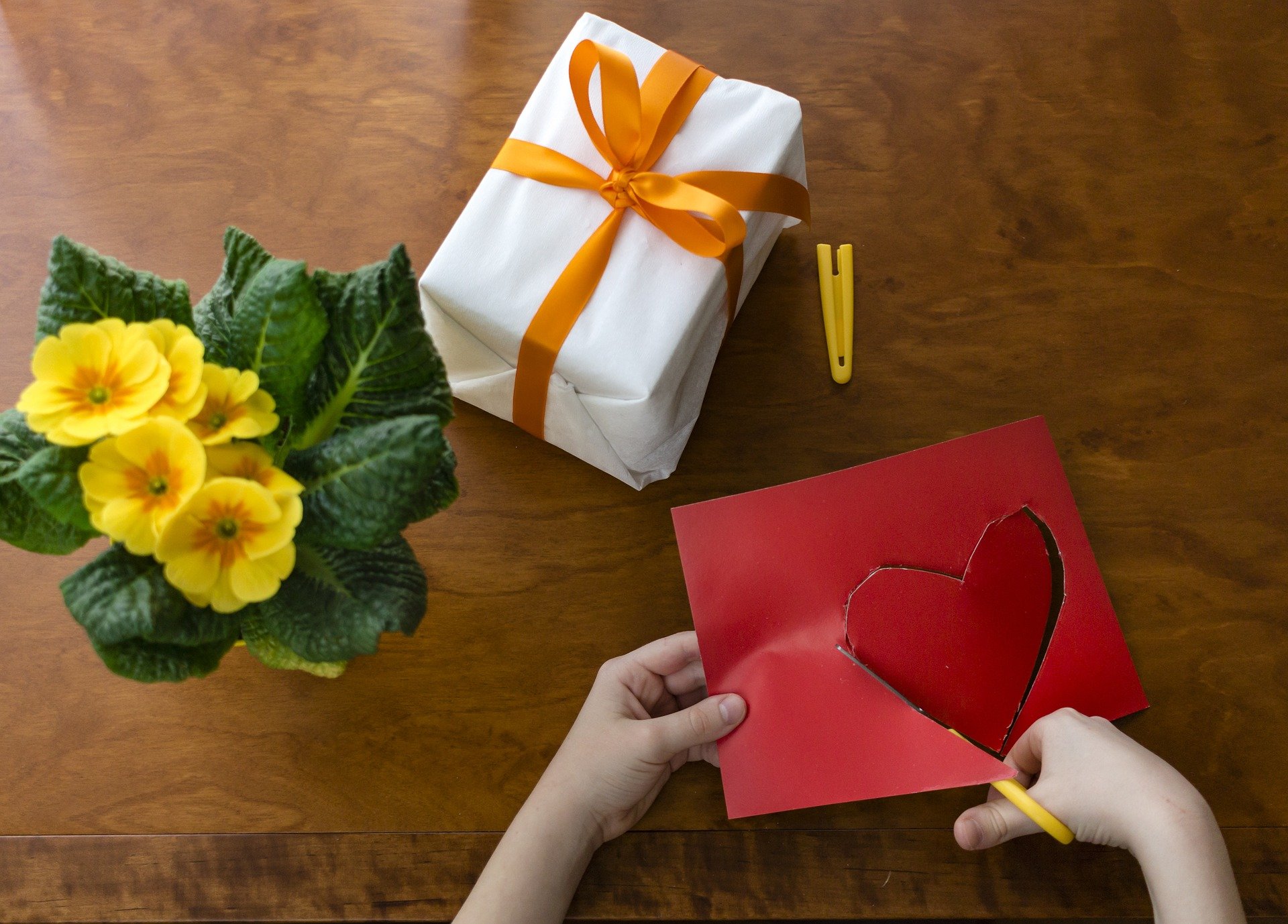 Pictured - A kid cutting out a heart shape next to wrapped gift and flowers | Source: Pixabay
