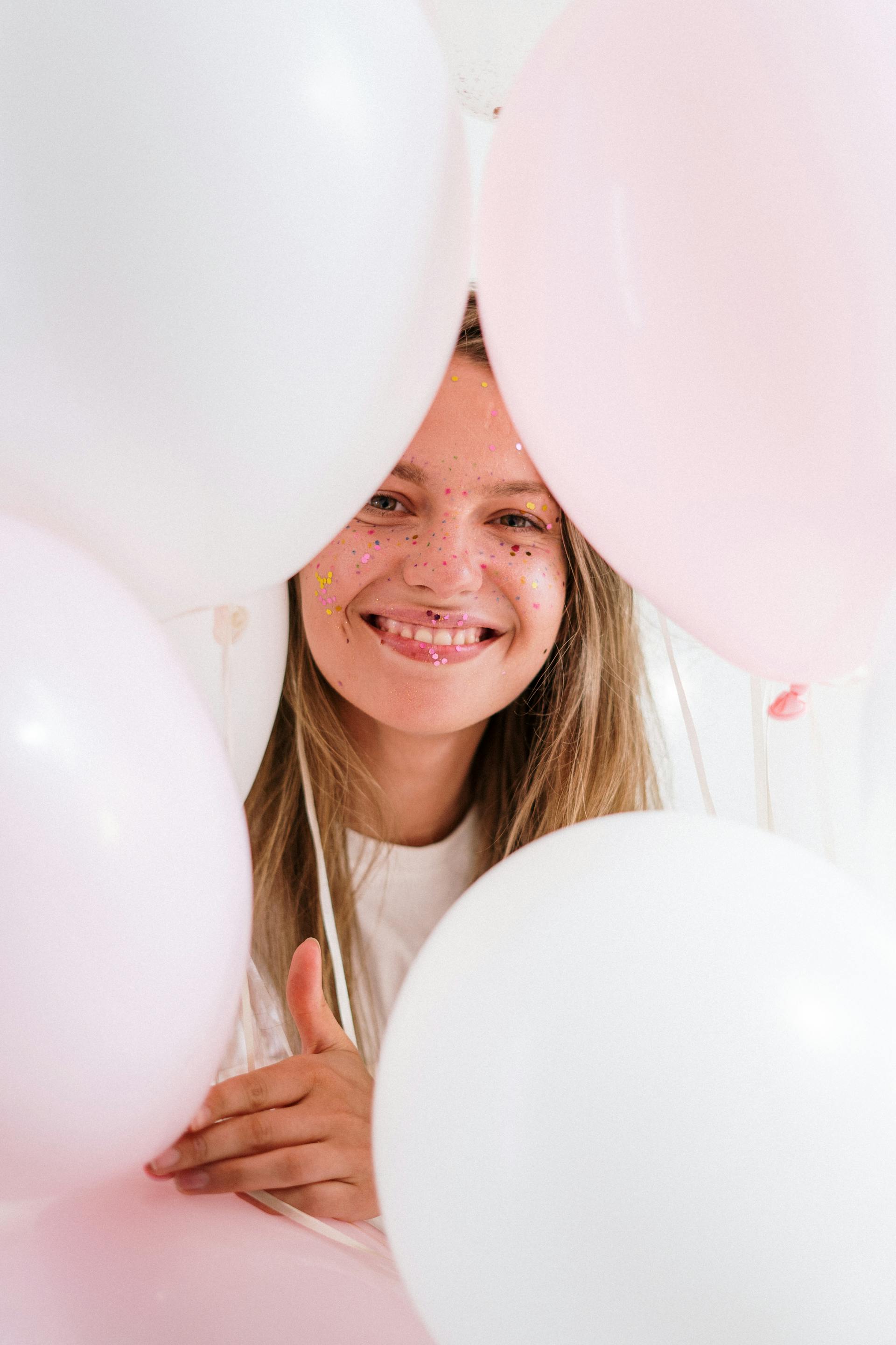 A smiling young girl holding pink and white balloons | Source: Pexels