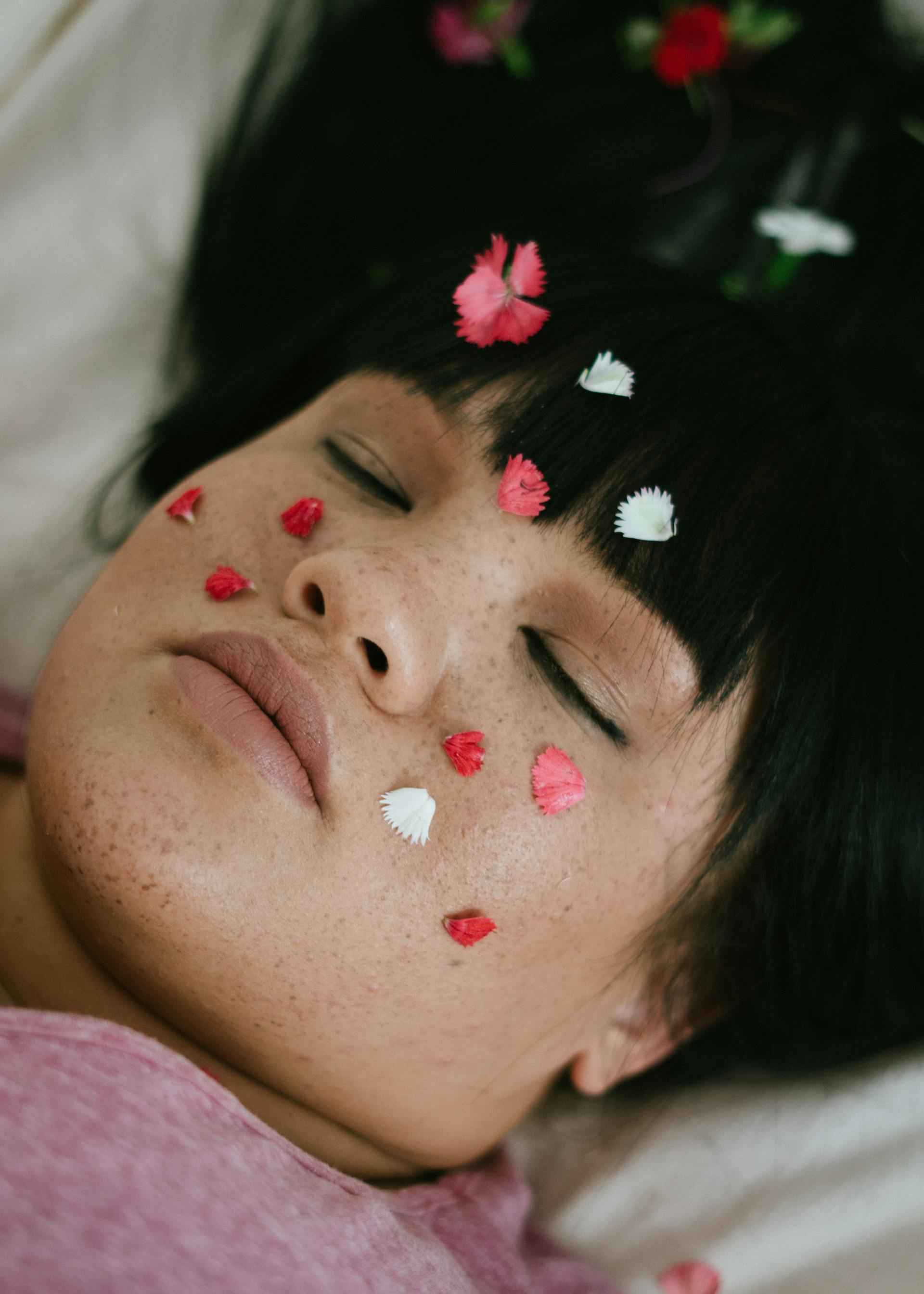A young woman lying with her eyes closed and rose petals on her face | Source: Pexels