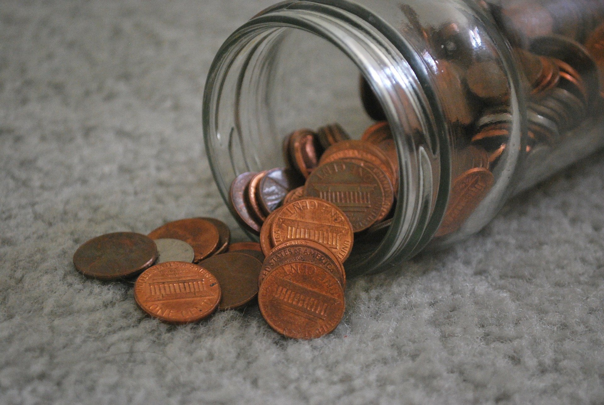 A jar of pennies spilling on to a carpet. | Photo: Pixabay/PublicDomainPictures