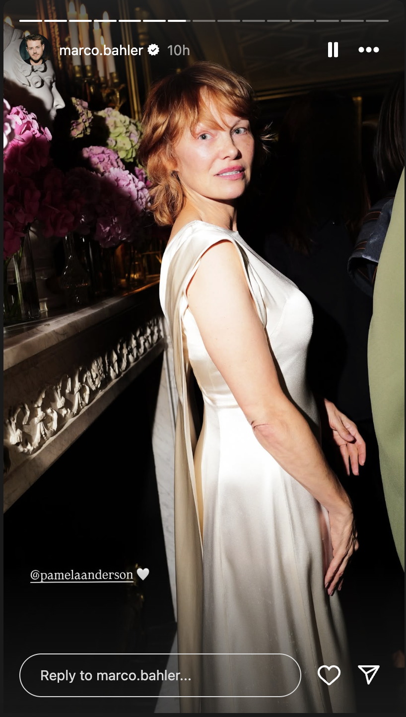 Pamela Anderson, with her red-copper hair styled in a short shaggy bob with bangs, wears a cream-colored, satin dress with a flowing back panel at Paris Fashion Week on September 29, 2025, in Paris, France | Source: Instagram/marco.bahler