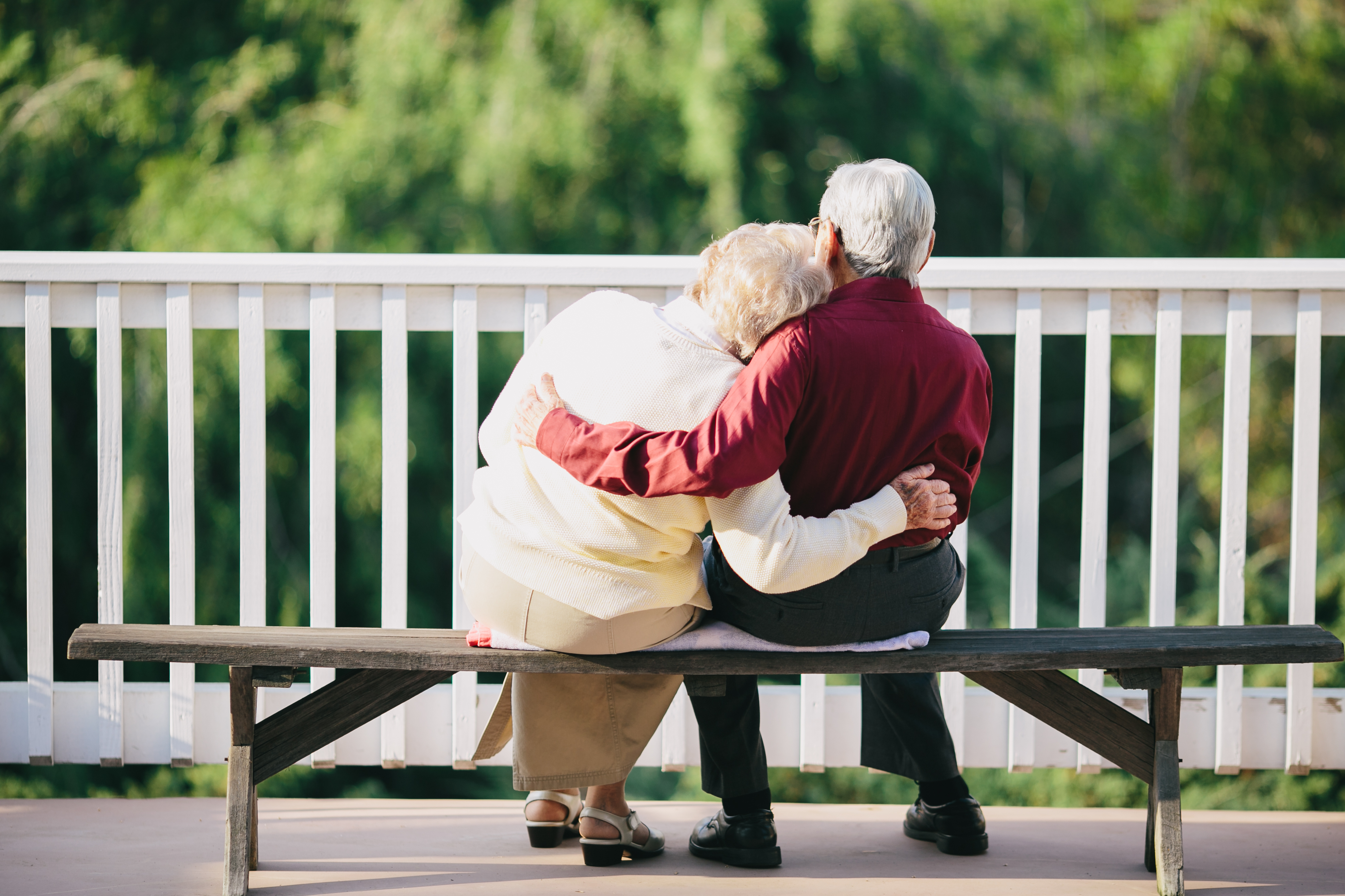 An elderly couple hugging while sitting on a bench outside | Source: Shutterstock
