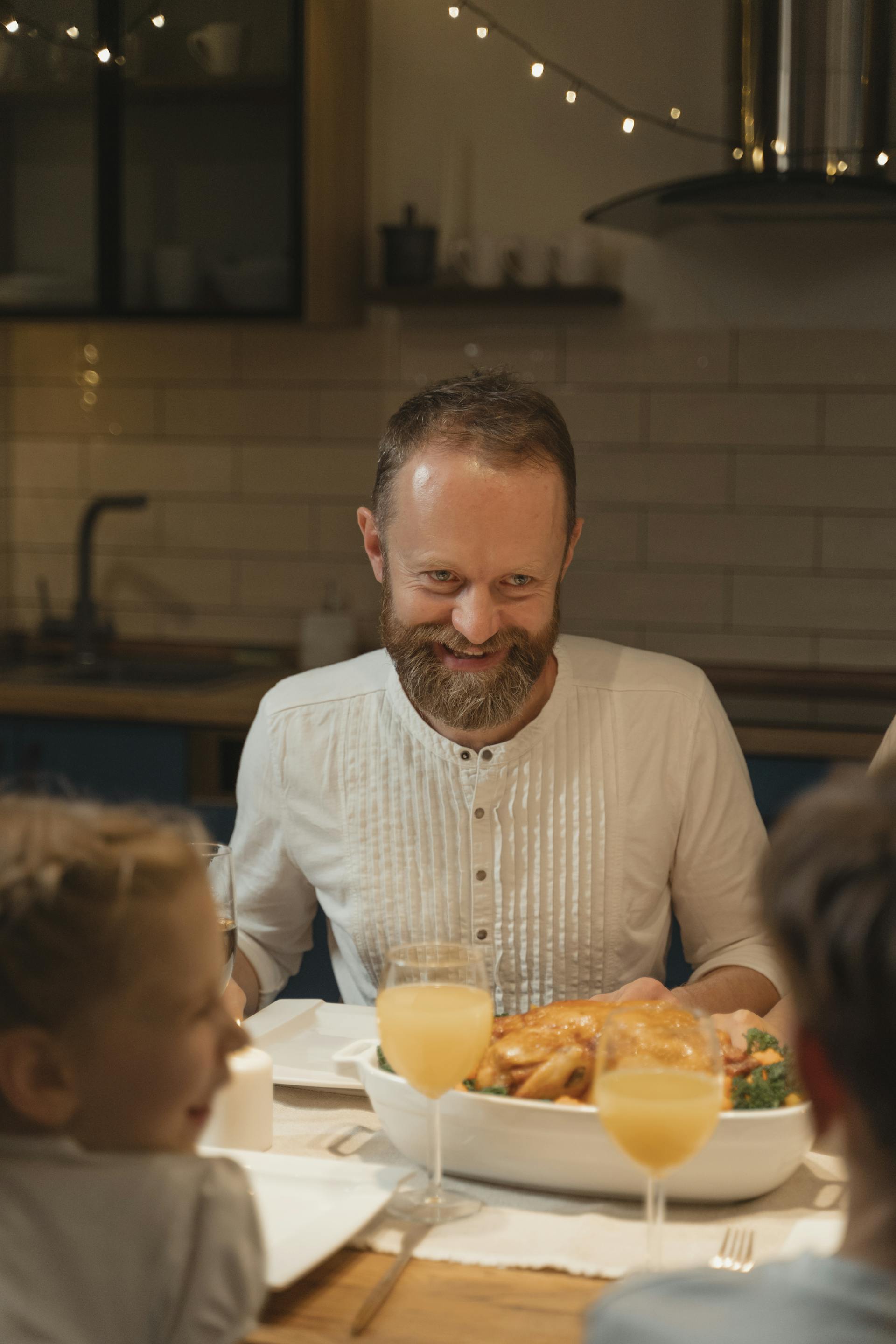 A bearded man smiles while sitting at the dinner table | Source: Pexels