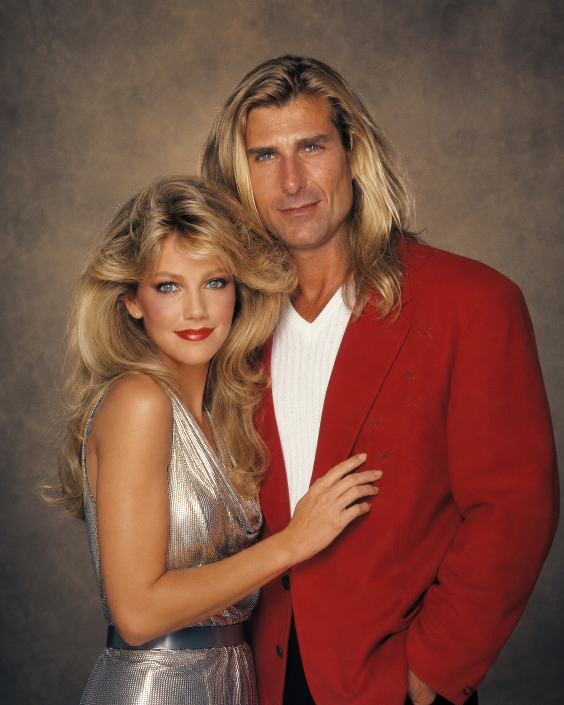 In an AI-generated portrait, Fabio wears a vibrant red blazer alongside Heather Locklear in a shimmering metallic dress, showcasing classic late 1980s celebrity glamour; the aesthetic strongly resembles Locklear's iconic "Melrose Place" era. | Source: ChatGPT