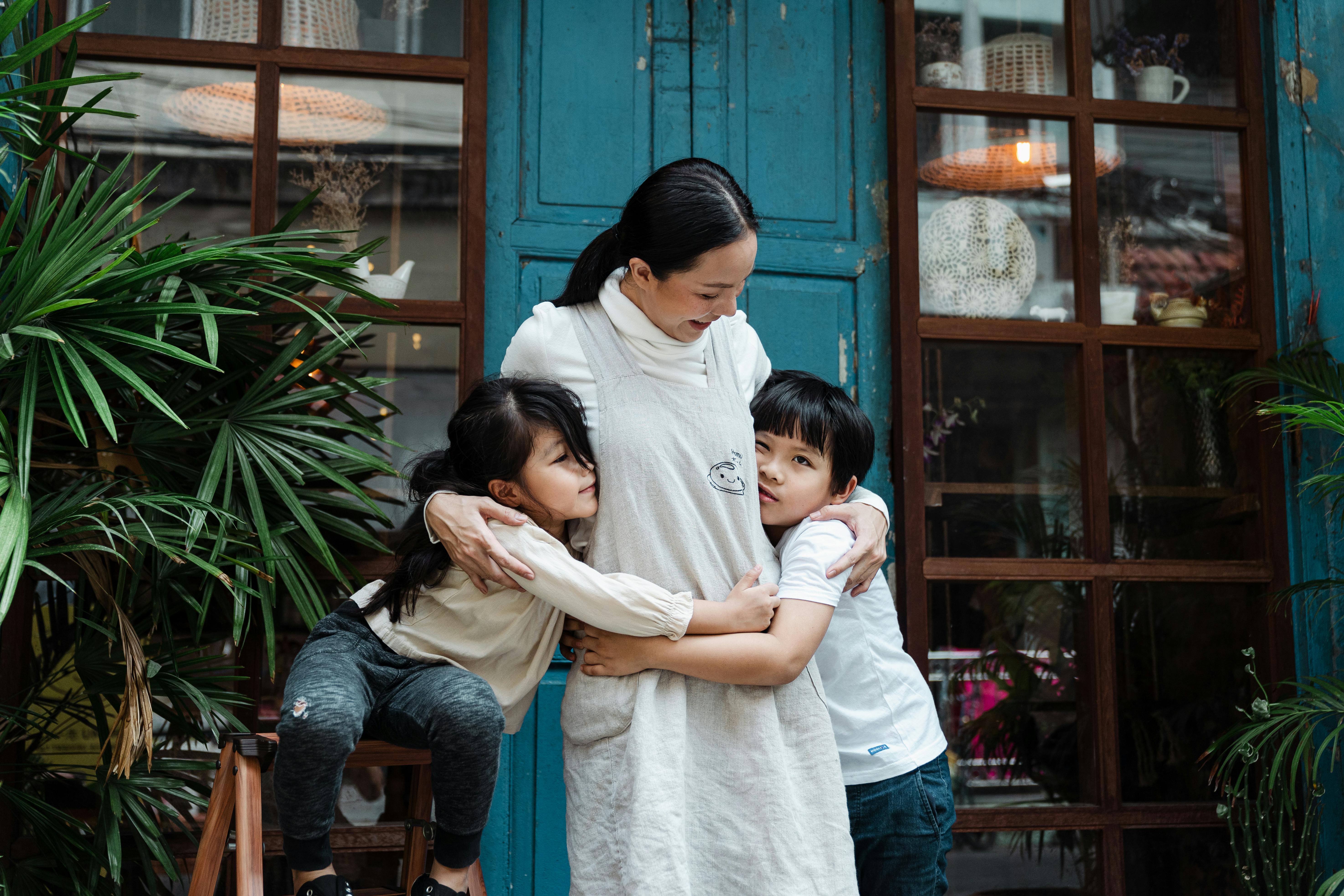 A woman embracing two young children | Source: Pexels