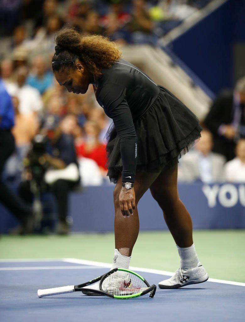 Serena Williams bends down to pick up her broken racket after throwing it to the ground in frustration during her 2018 US Open Finals match against Naomi Osaka in September 8, 2018. | Photo: Getty Images