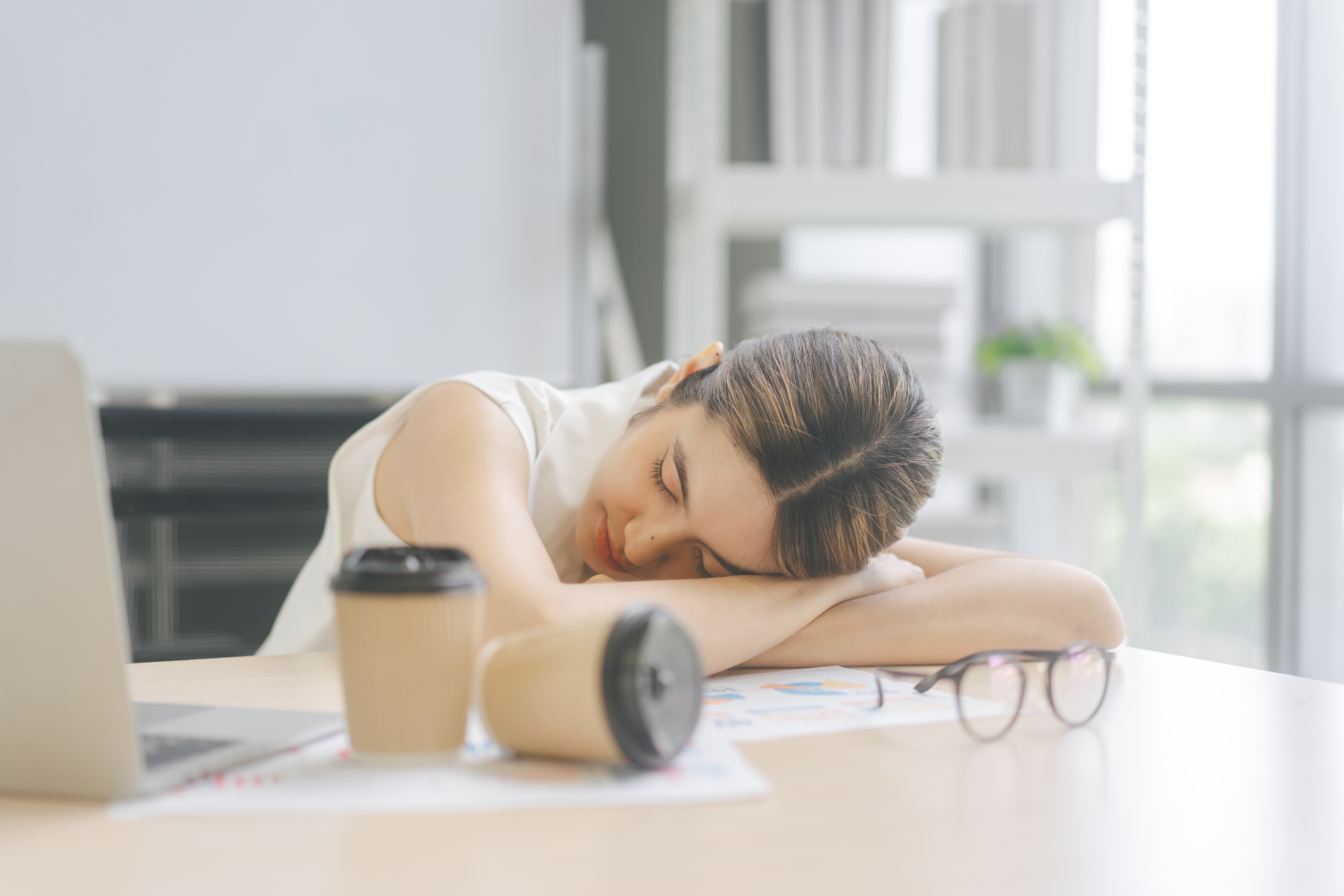 A tired young woman sleeps on the table with cups of coffee  | Source: Shutterstock