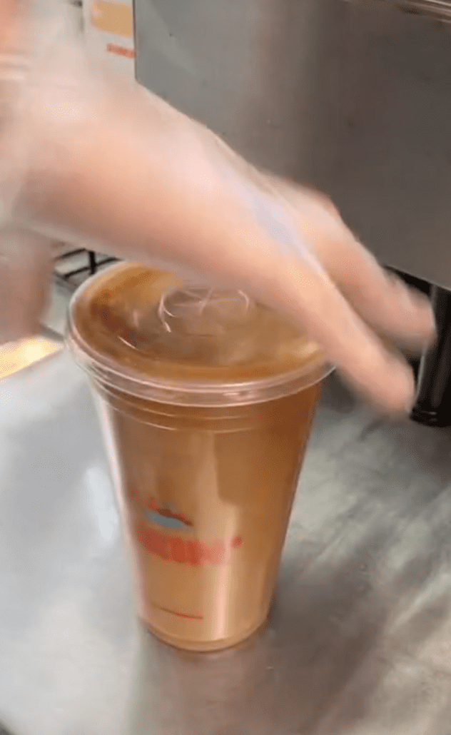 Dunkin' employee picks up a drink and shakes it with his hand showing viewers how he makes drinks for non-tipping customers | Photo: TikTok/jasonmora2