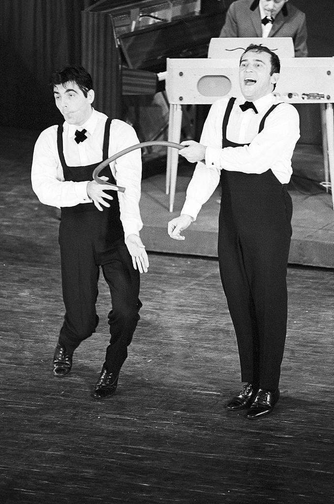 Le duo comique Roger PIERRE (à gauche) et Jean-Marc THIBAULT interprétant l'un de leur sketch, portant tous les deux des pantalons salopette et un noeud papillon. | Photo : Getty Images
